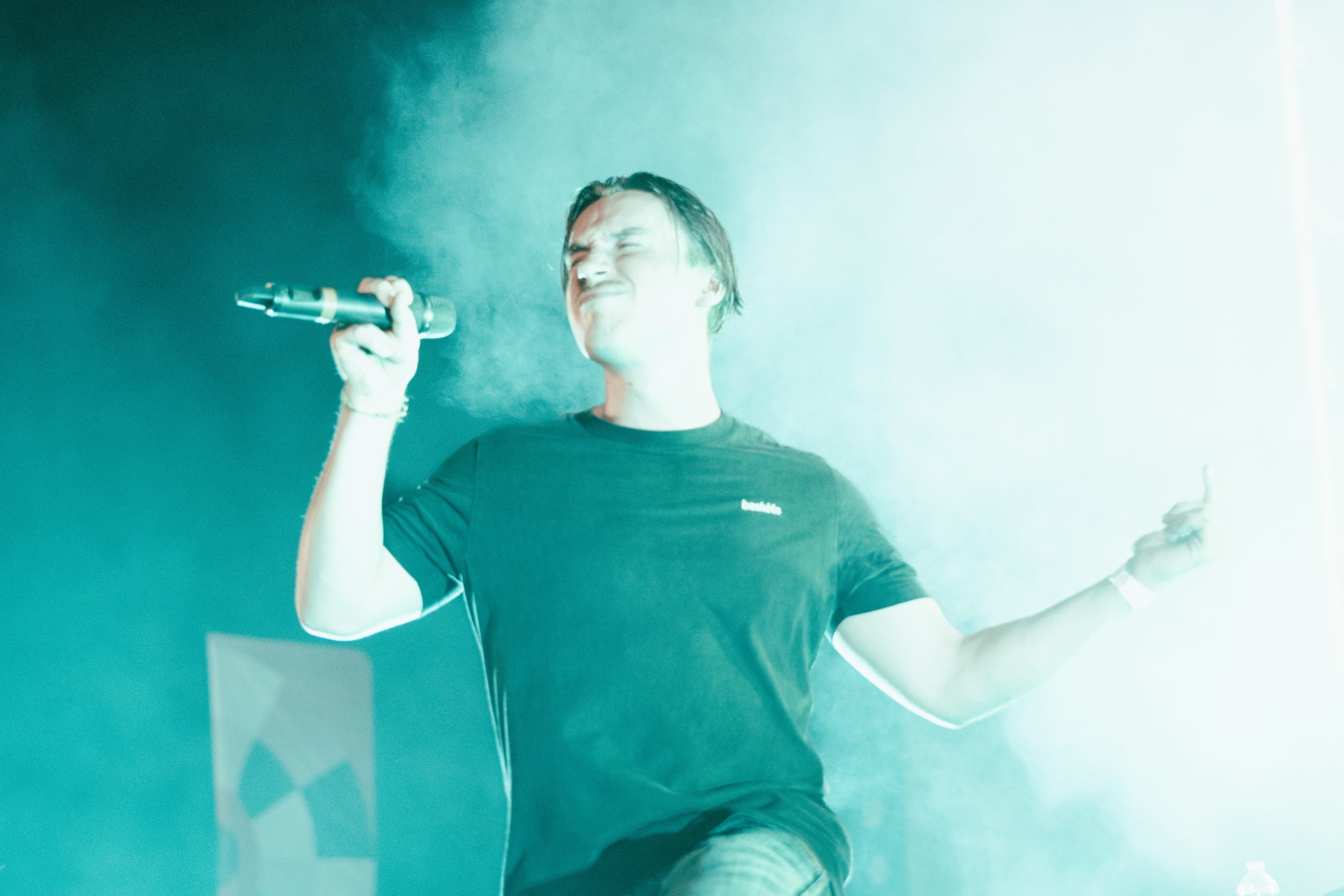 Un homme chante en tenant un microphone, dans une ambiance lumineuse avec de la fumée.