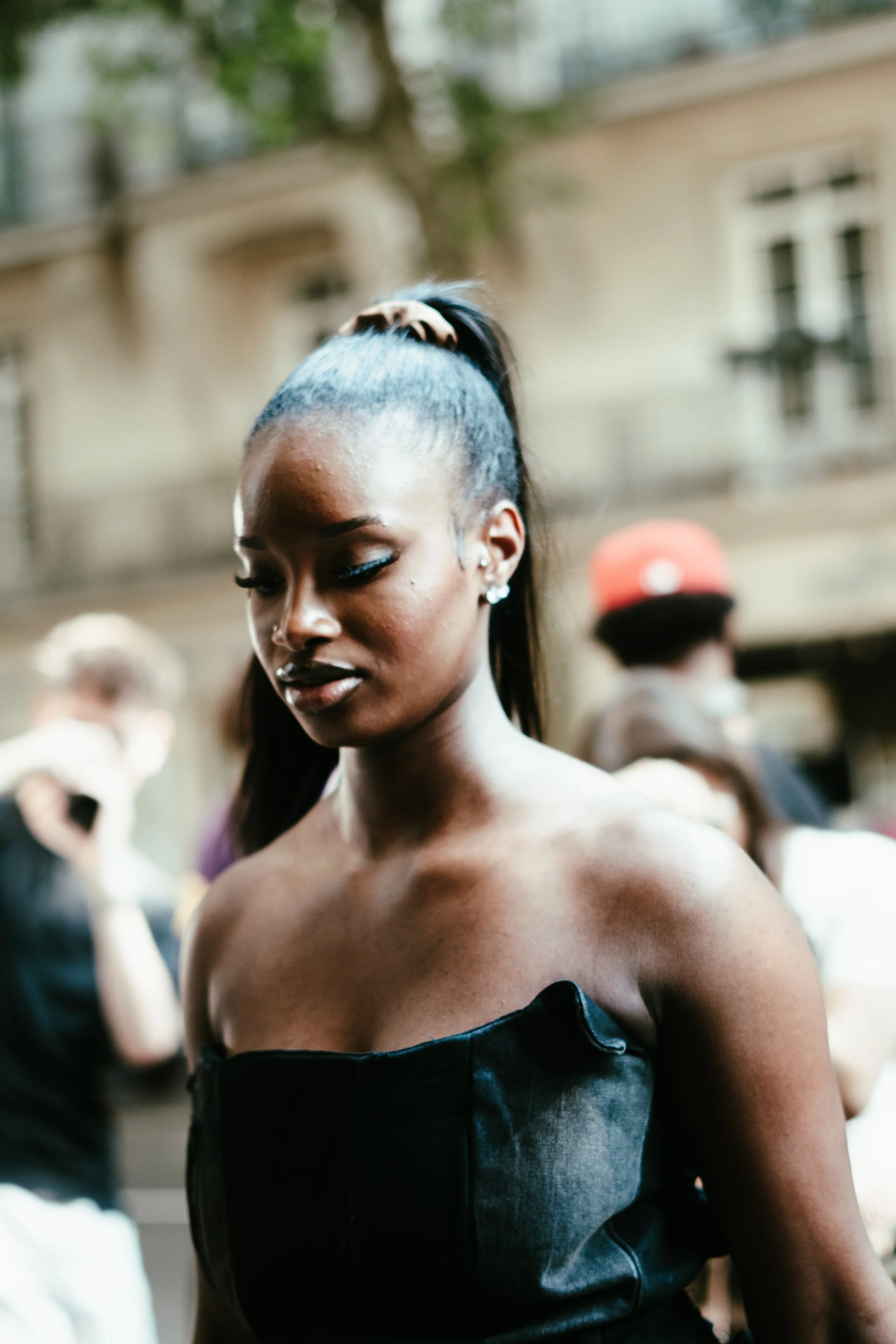 Une femme noire élégante avec une queue de cheval, portant un haut en cuir noir, dans une foule en plein air.
