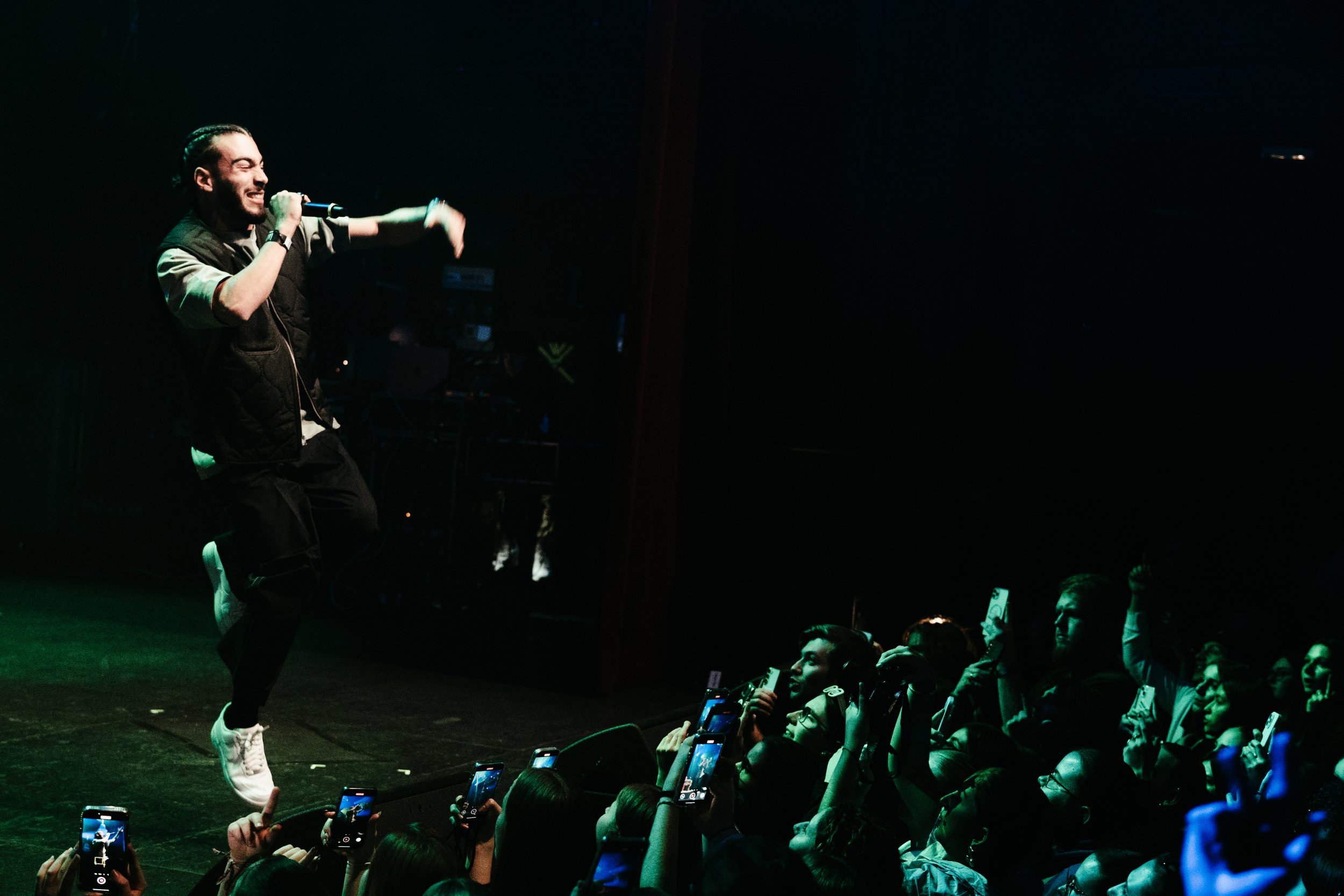 Un artiste de danse en train de performer sur scène devant un public qui le filme et l'admire, dans une ambiance sombre avec des lumières vertes.