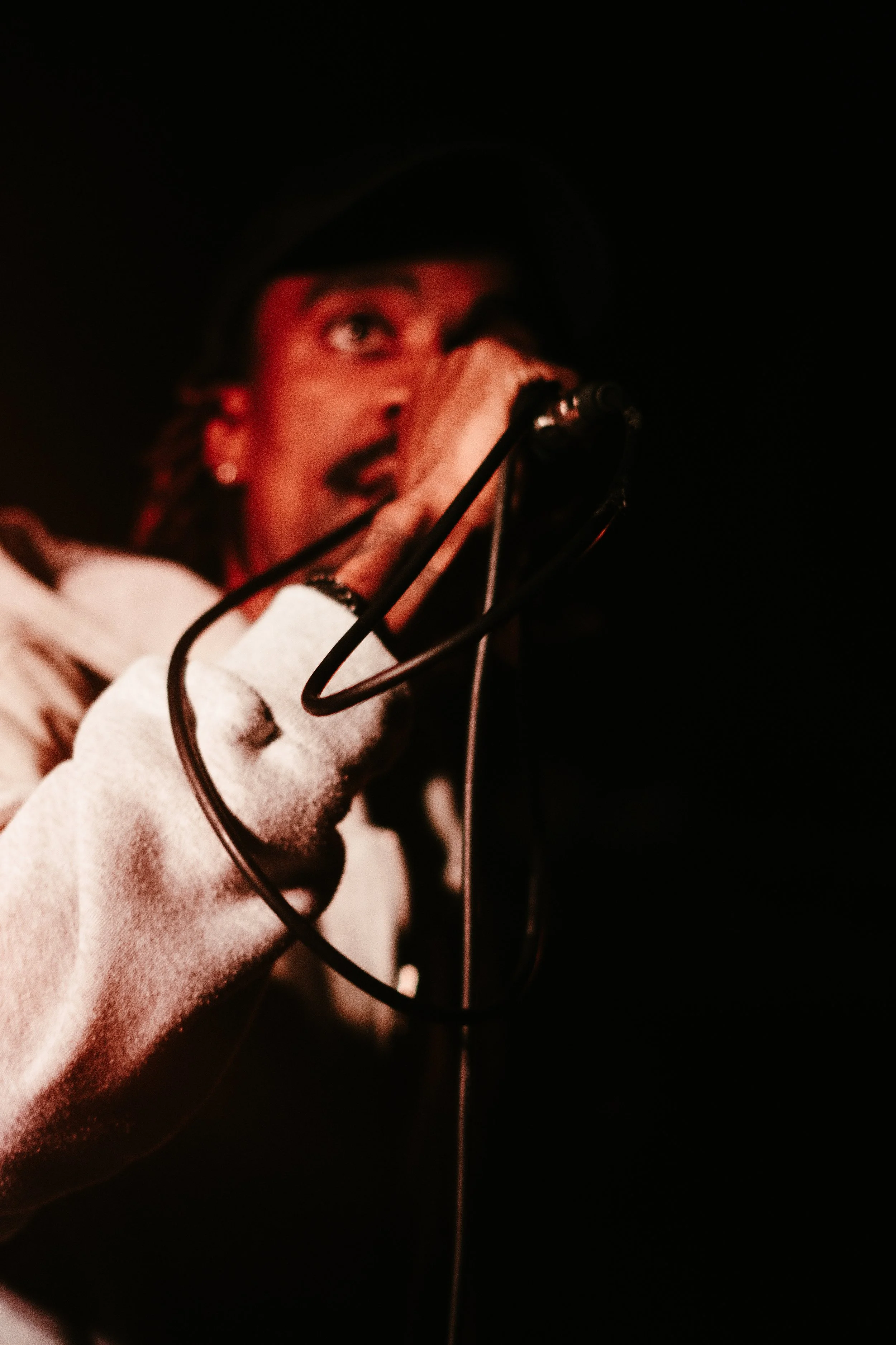 Un chanteur en chemise blanche, portant un gant blanc, chante dans un microphone contre un fond noir, avec une expression passionnée.