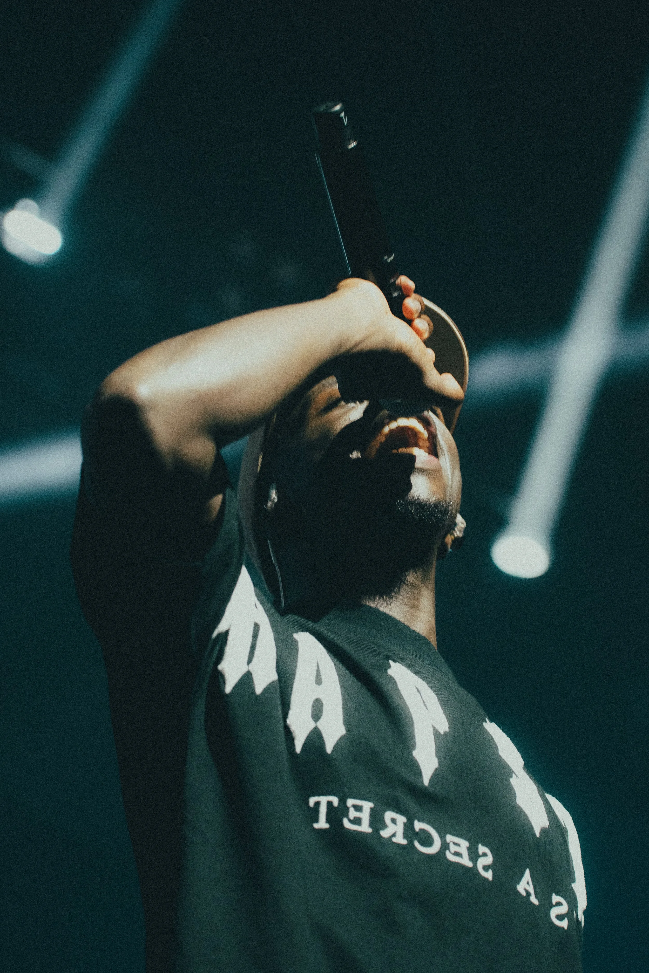 Un homme chante en tenant un micro, avec un casque sur la tête, sur scène avec des lumières de spectacle.