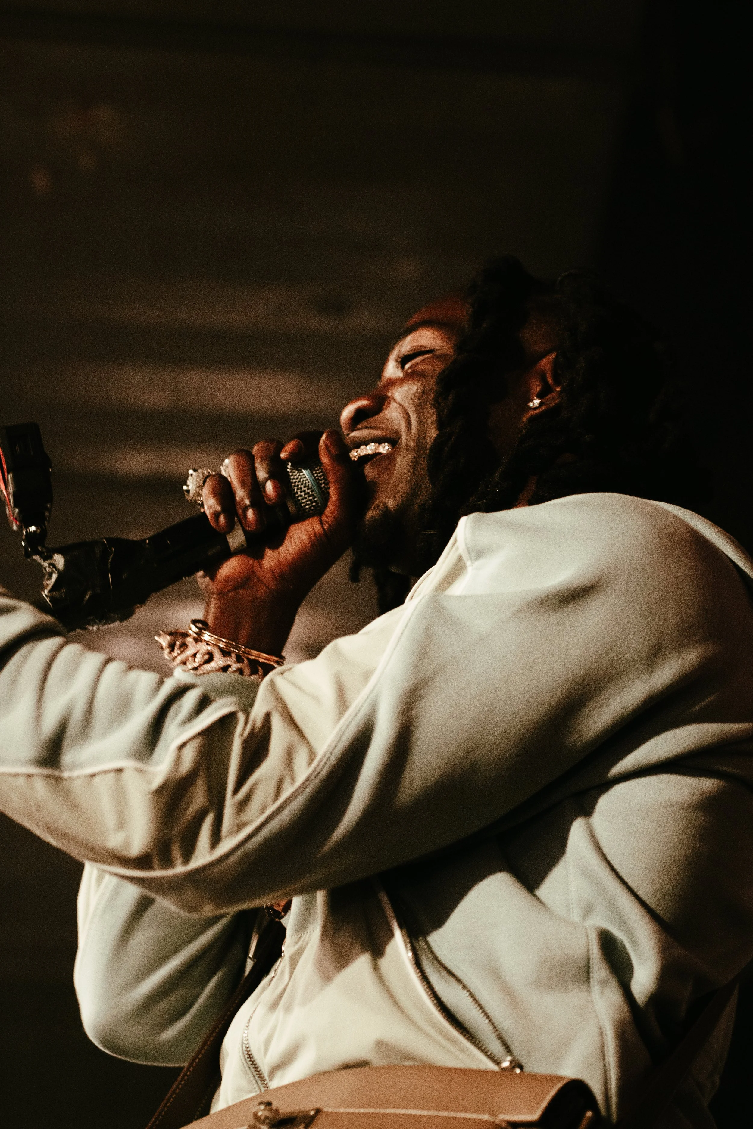 Un homme chante en souriant, tenant un microphone dans la main, avec des cheveux bouclés ou dreadlocks.