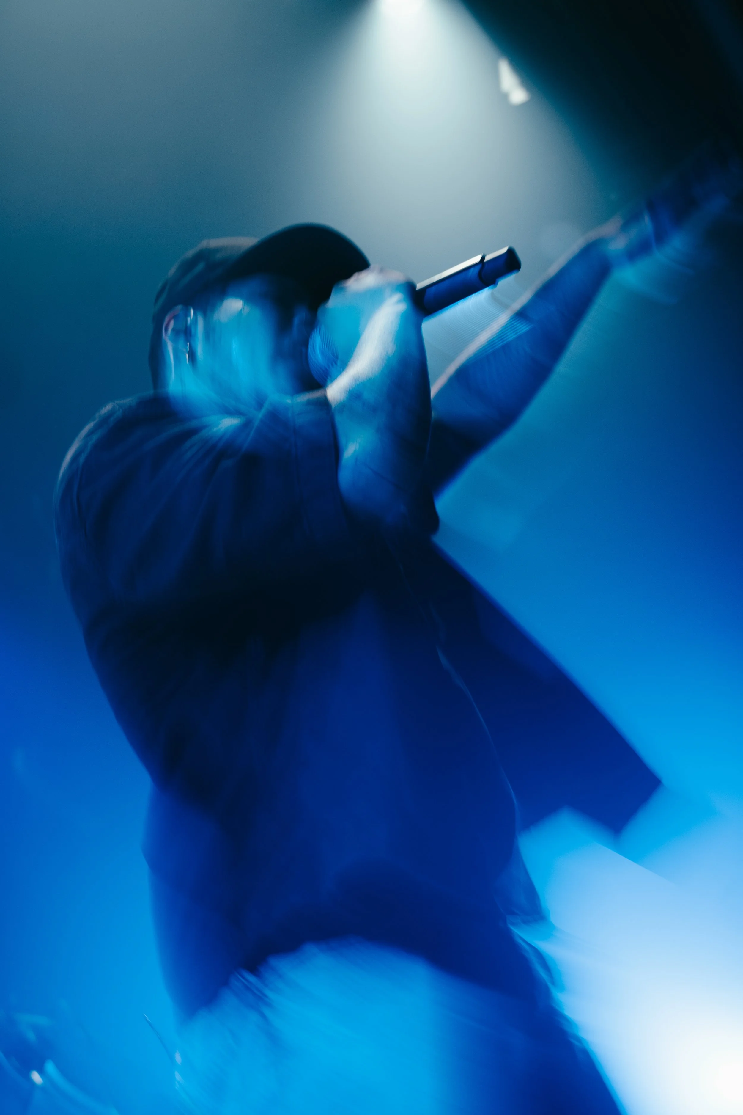 Une personne tenant un microphone et chantant sur scène, éclairée par des lumières bleues et blanches, avec un effet de flou artistique.