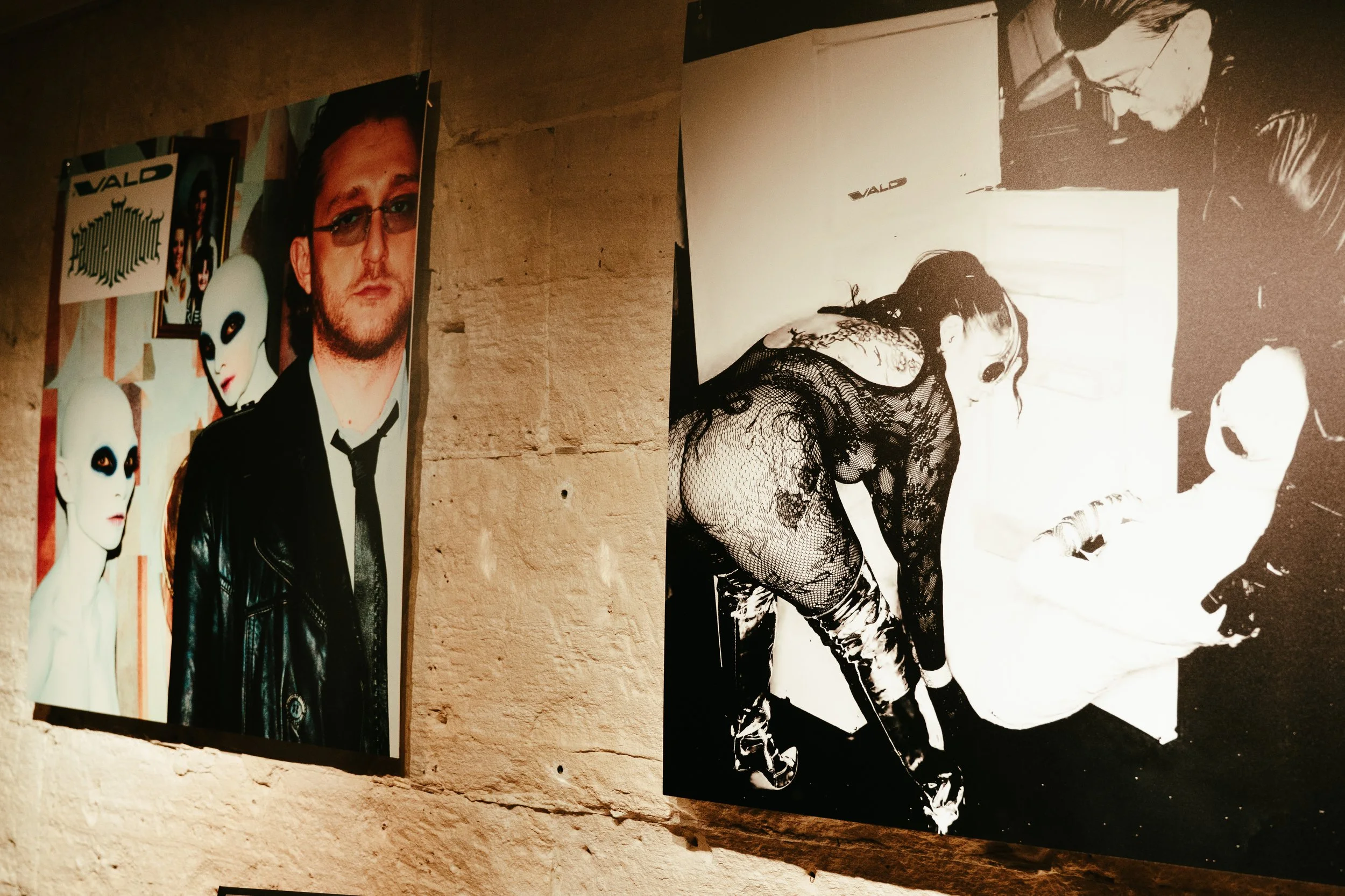 Photographies exposées sur un mur en pierre, l'une montre un homme avec un costume noir et deux mannequins avec des visages sans traits, l'autre montre une femme en vêtements en dentelle et des personnes dans un environnement intérieur.