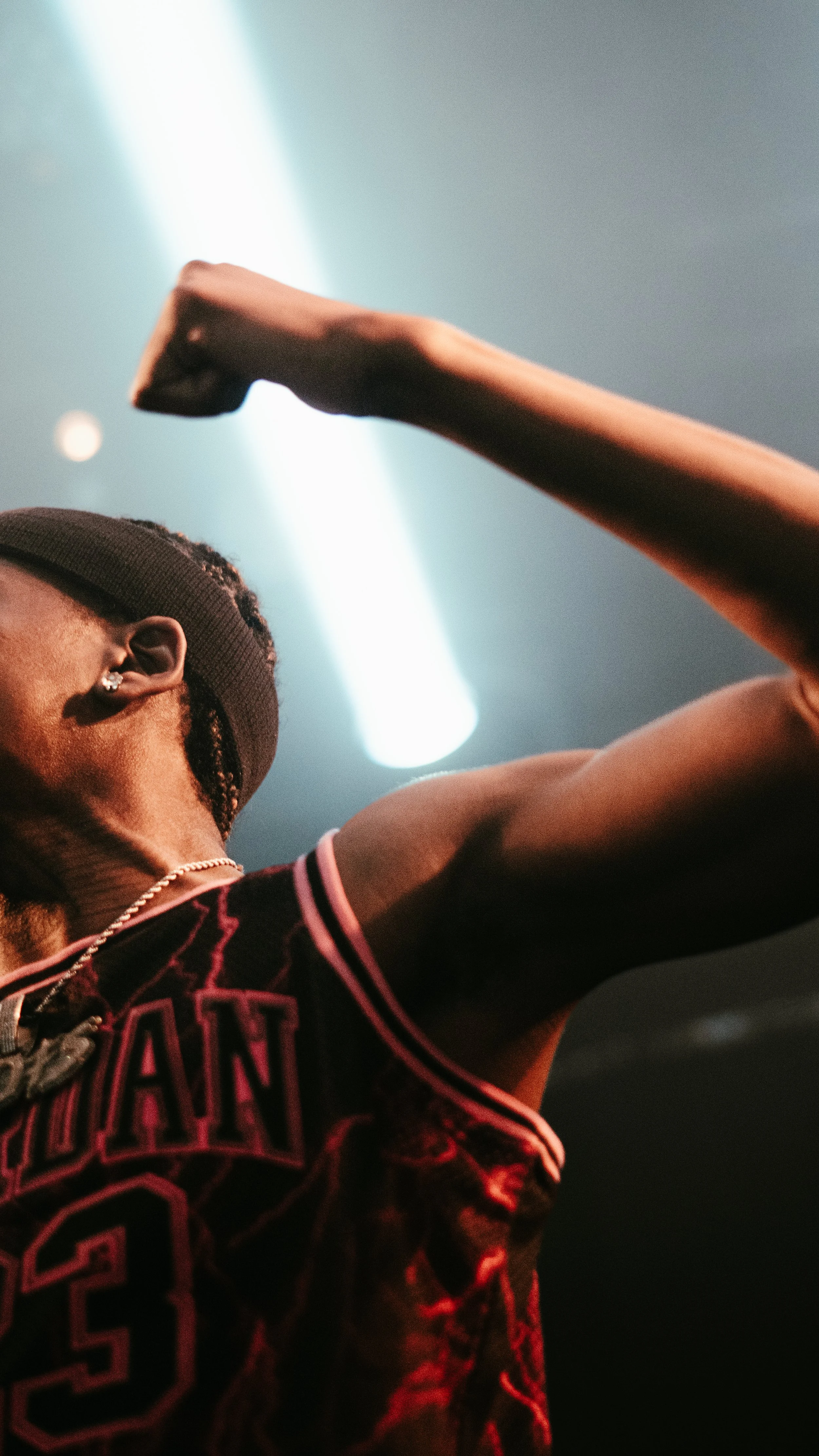 Une personne en mouvement lors d'une performance ou d'une danse, portant un maillot sans manches et une casquette, avec un éclairage de scène en arrière-plan.