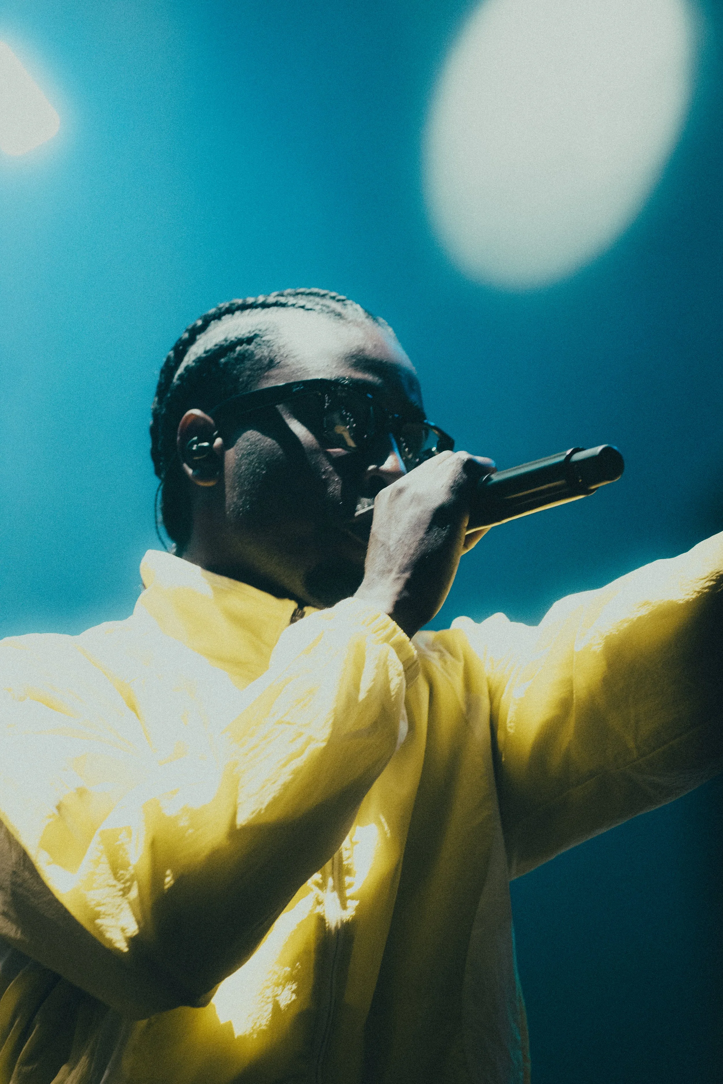 Une personne portant des lunettes de soleil et une veste jaune, tenant un microphone et chantant en spectacle.