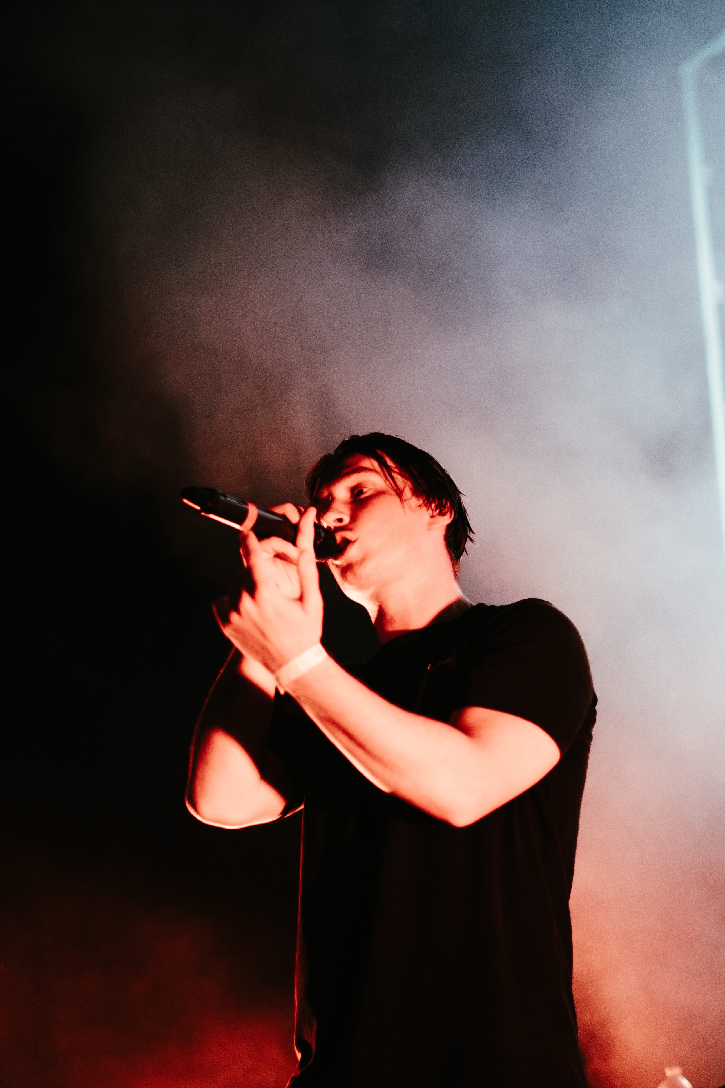 Une personne chante dans un microphone, éclairée par des lumières rouges et des effets de fumée, lors d'une performance sur scène.