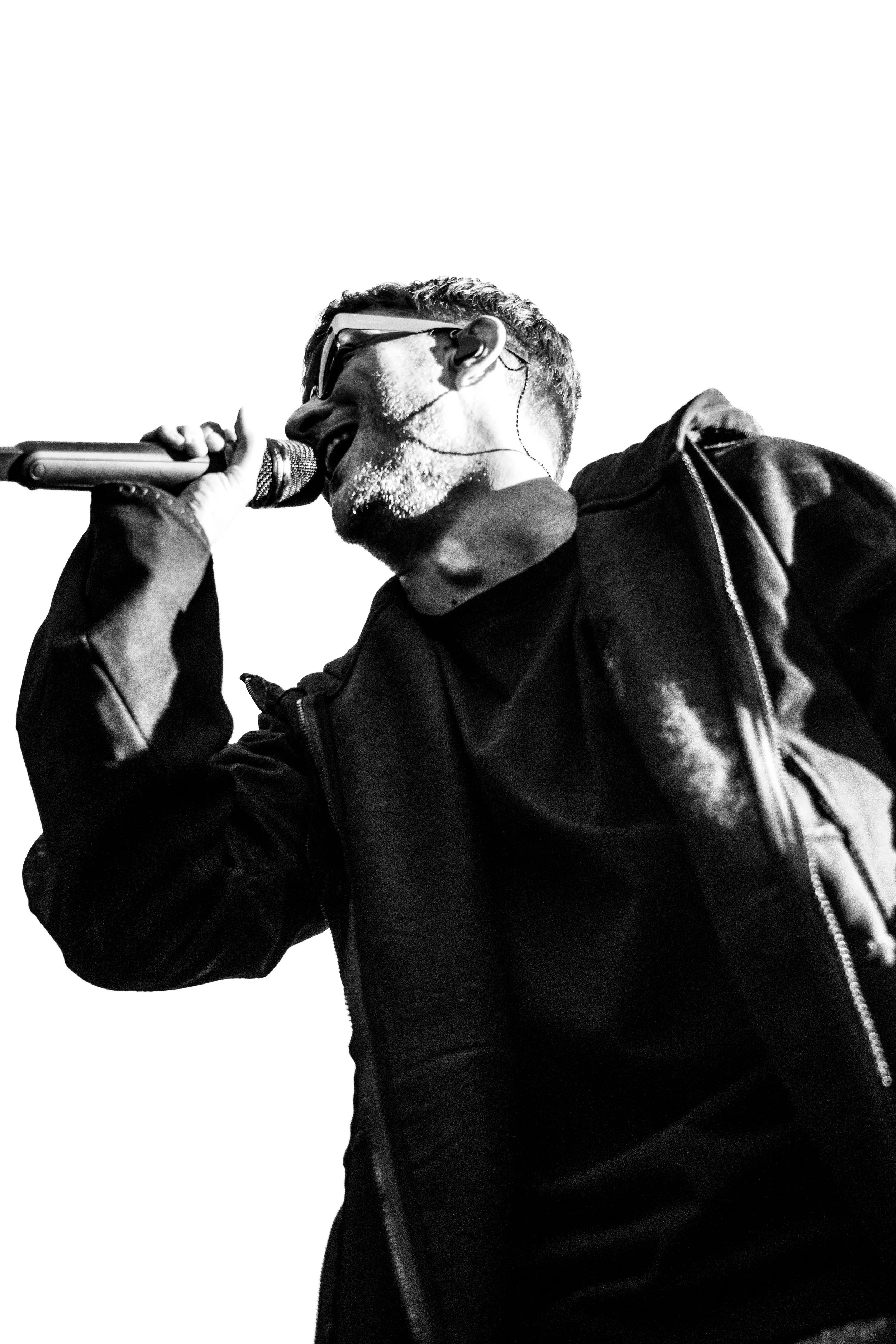 Homme chantant avec un microphone, portant des lunettes de soleil et un casque d'écoute, en noir et blanc.