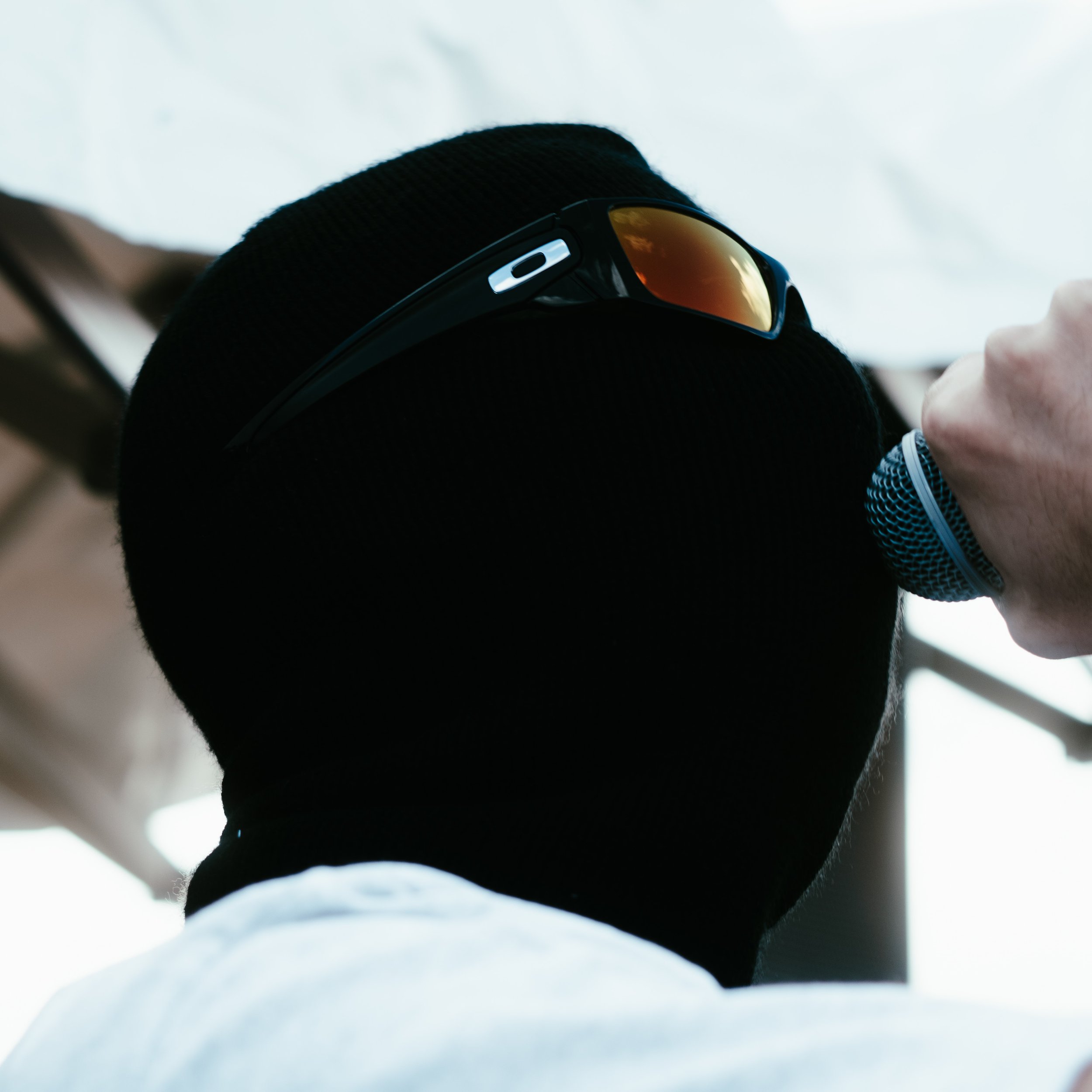 Une personne portant un masque noir, des lunettes de soleil sur la tête, tenant un microphone à la main.