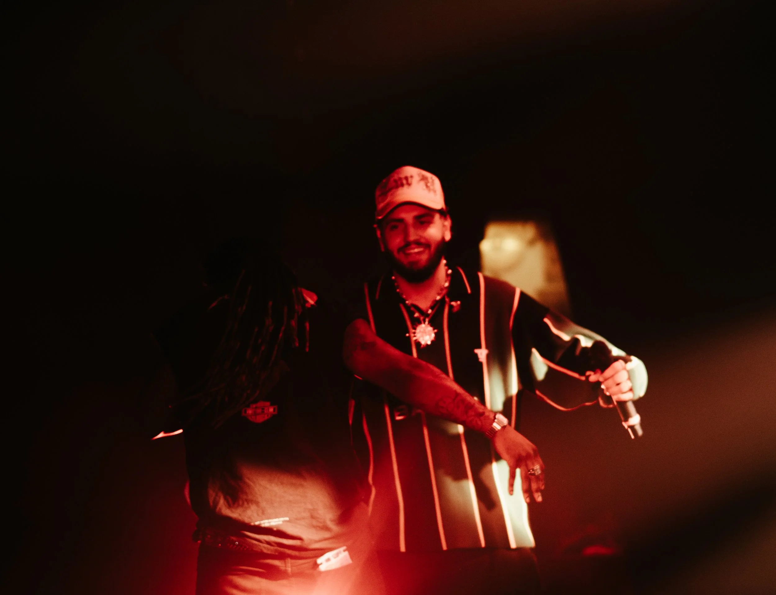 Deux personnes souriantes, une homme tenant un microphone dans un environnement sombre avec un éclairage rouge