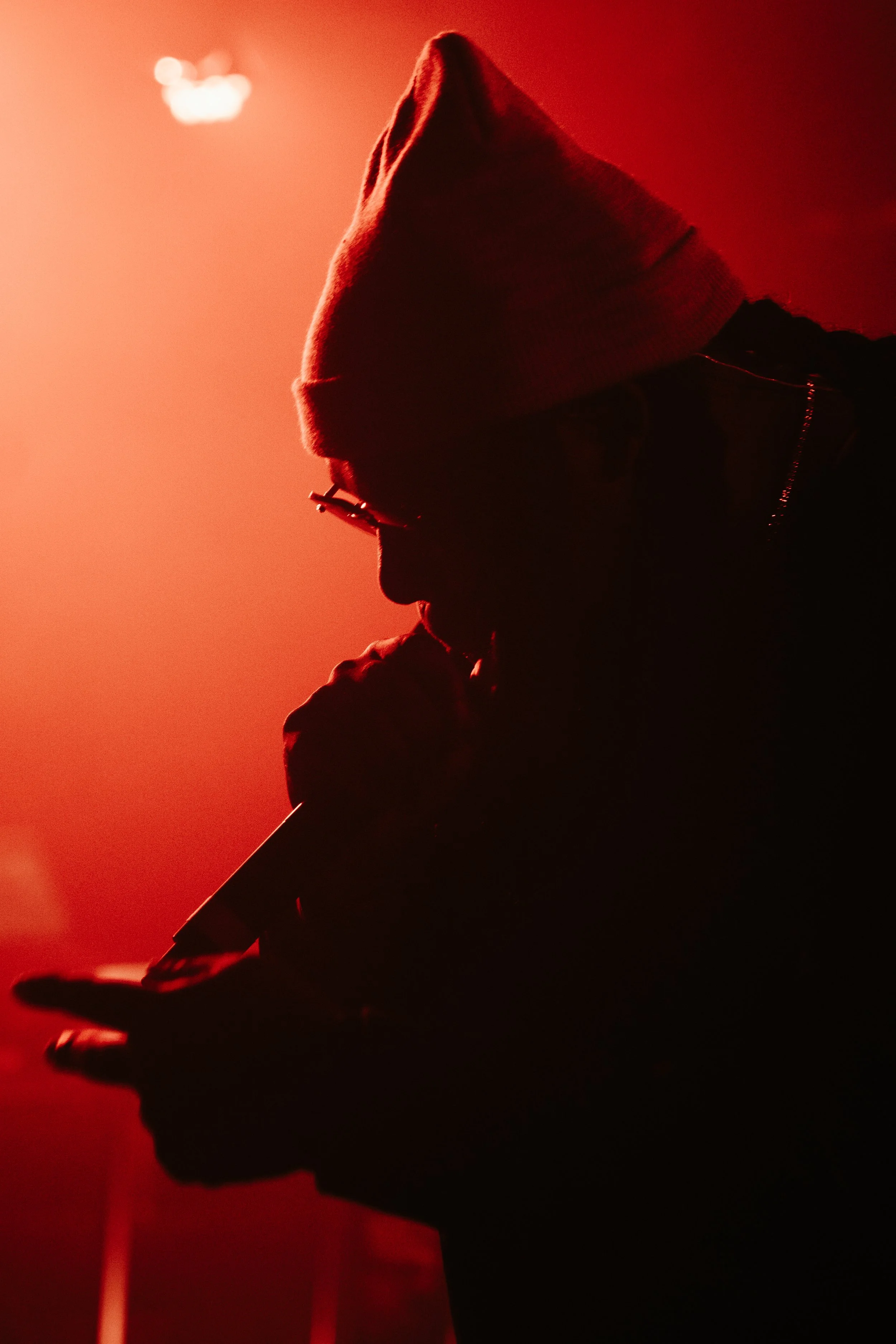 Silhouette d'une personne portant un bonnet, avec un environnement rouge en arrière-plan, tenant un micro.