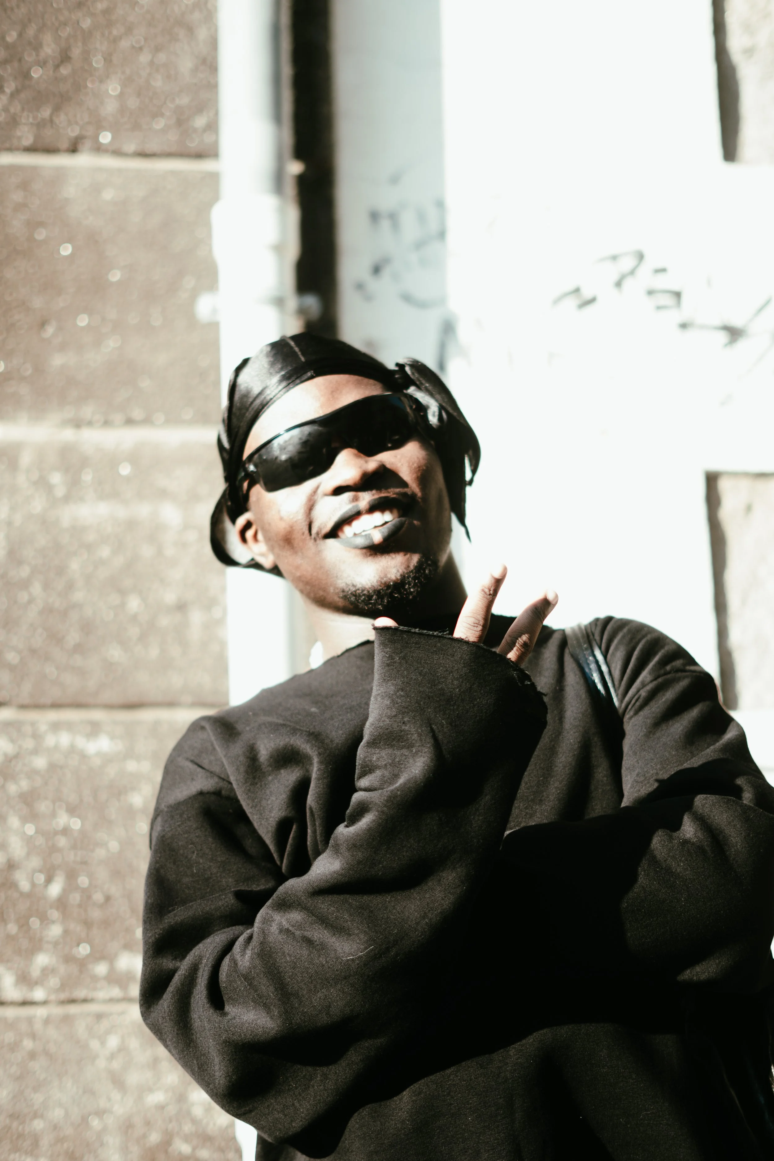 Jeune homme portant des lunettes de soleil et un bonnet noir, posant avec un geste de paix.