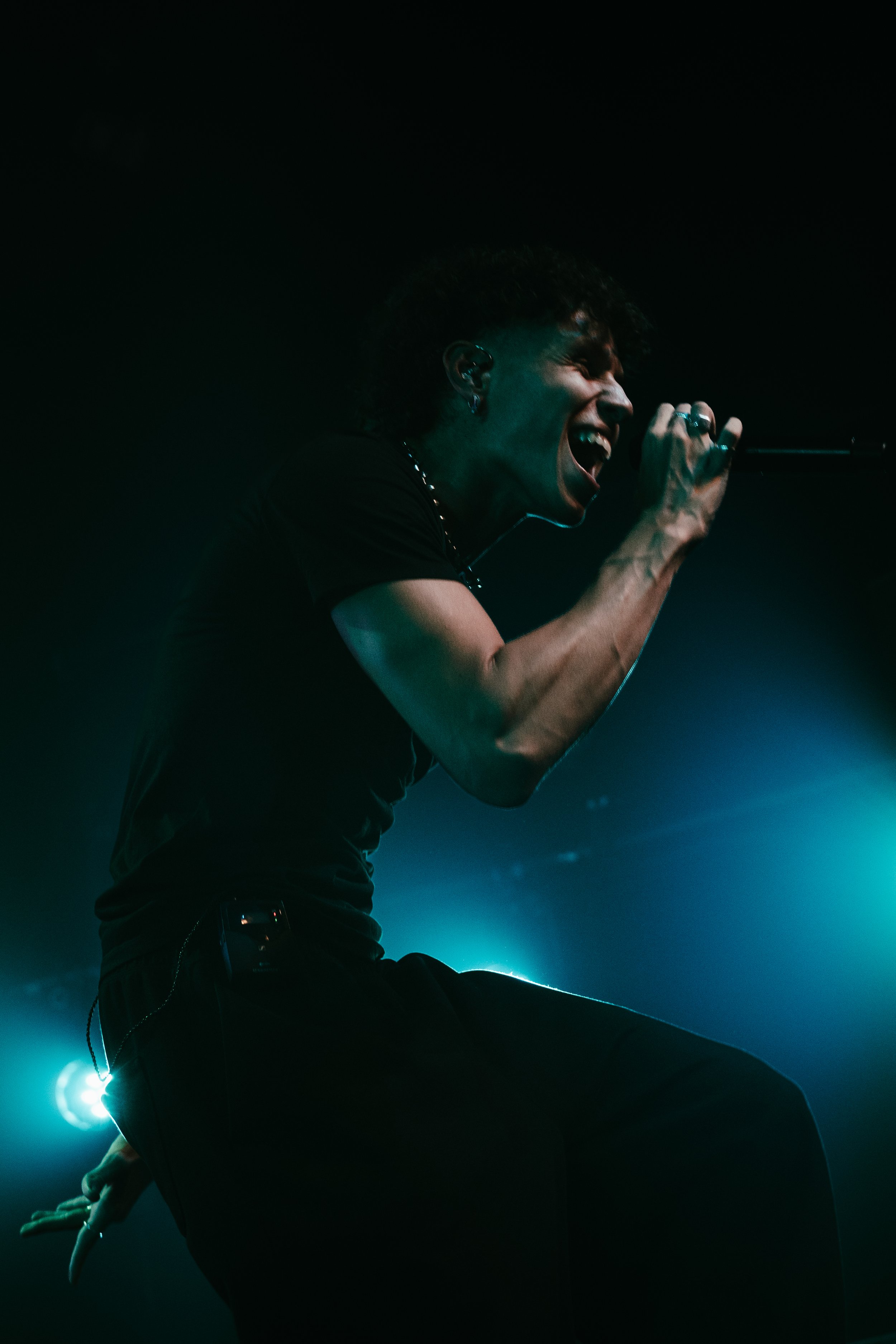 Un chanteur masculin en train de performer sur scène dans une atmosphère sombre avec des éclairages bleus.