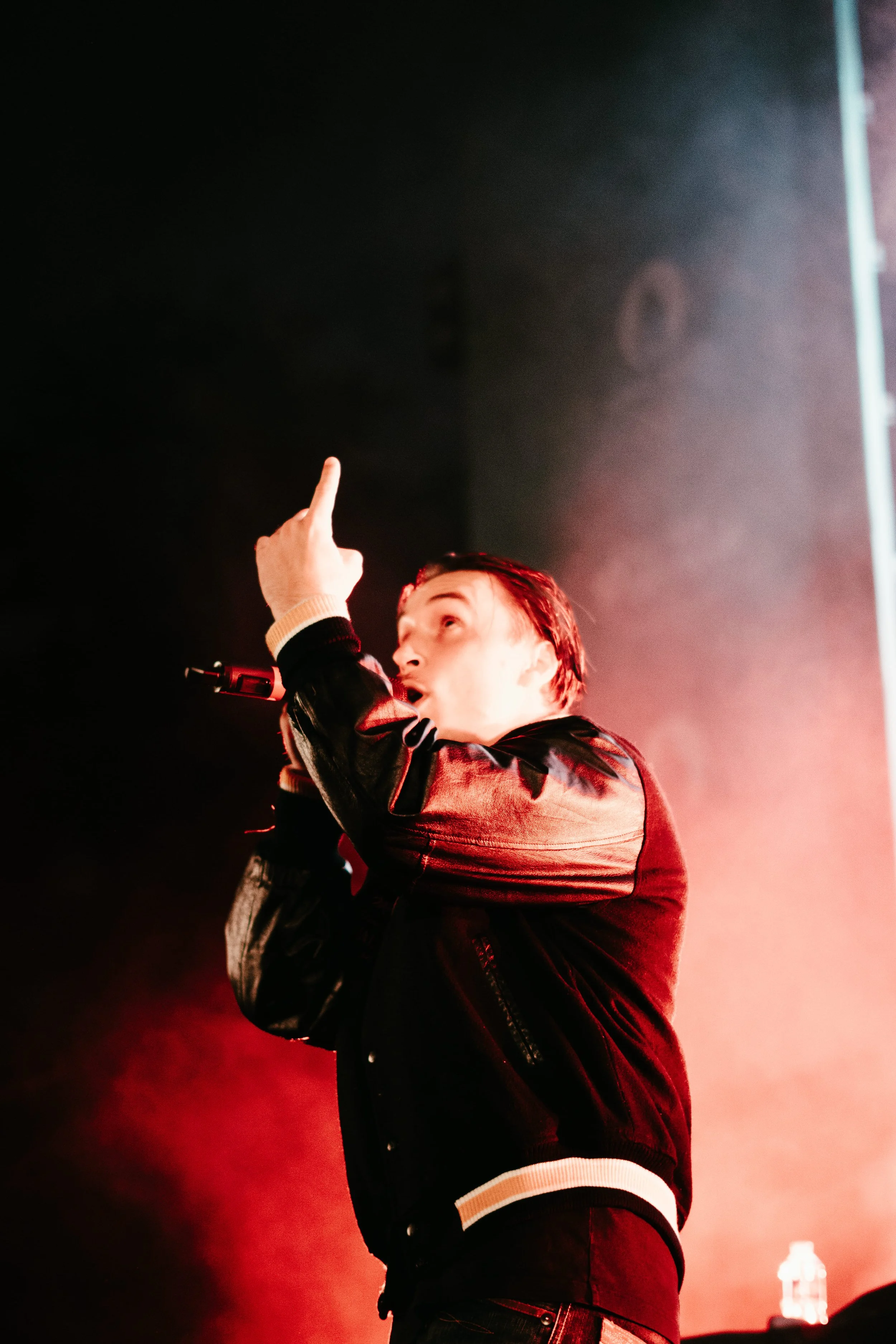 Un homme qui chante ou parle en microphone sur scène, levant un doigt.