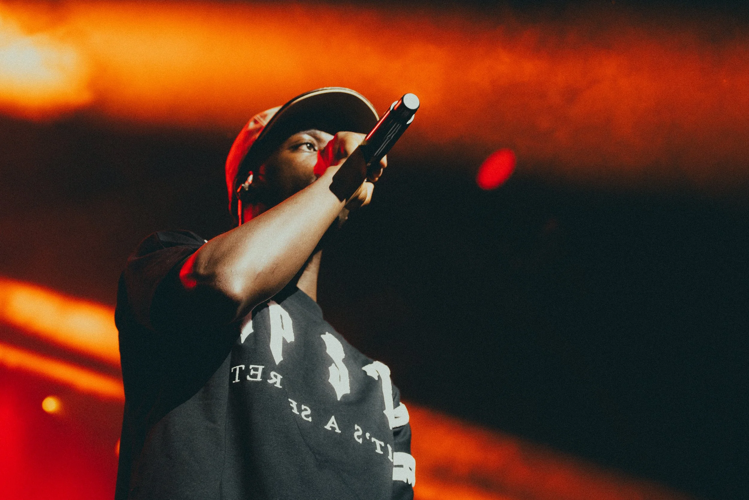 Un artiste de rap en performance sur scène, portant une casquette et un t-shirt noir, tenant un microphone.