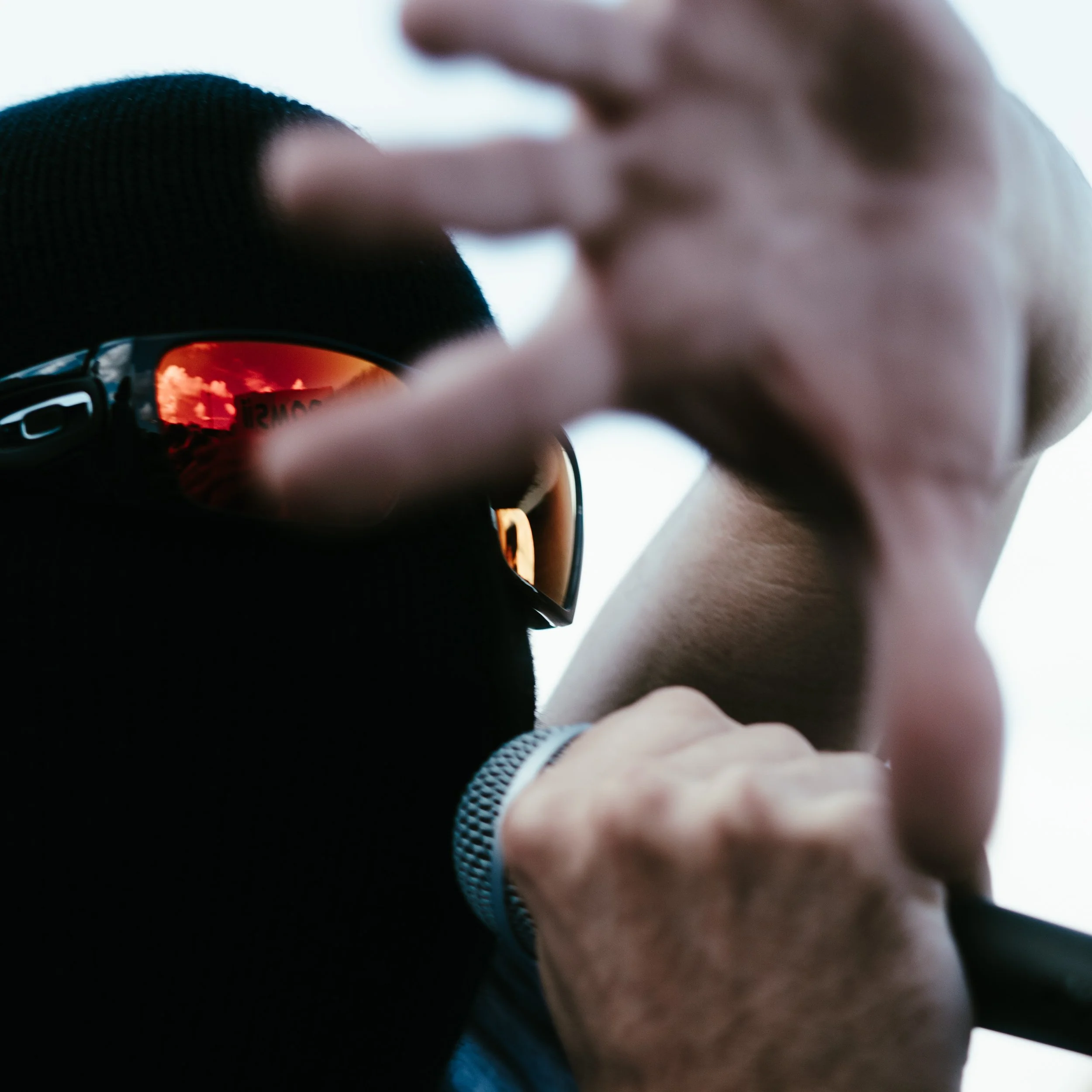 Personne portant des lunettes de soleil à miroir rouge, en train de faire un geste avec la main, vue rapprochée.