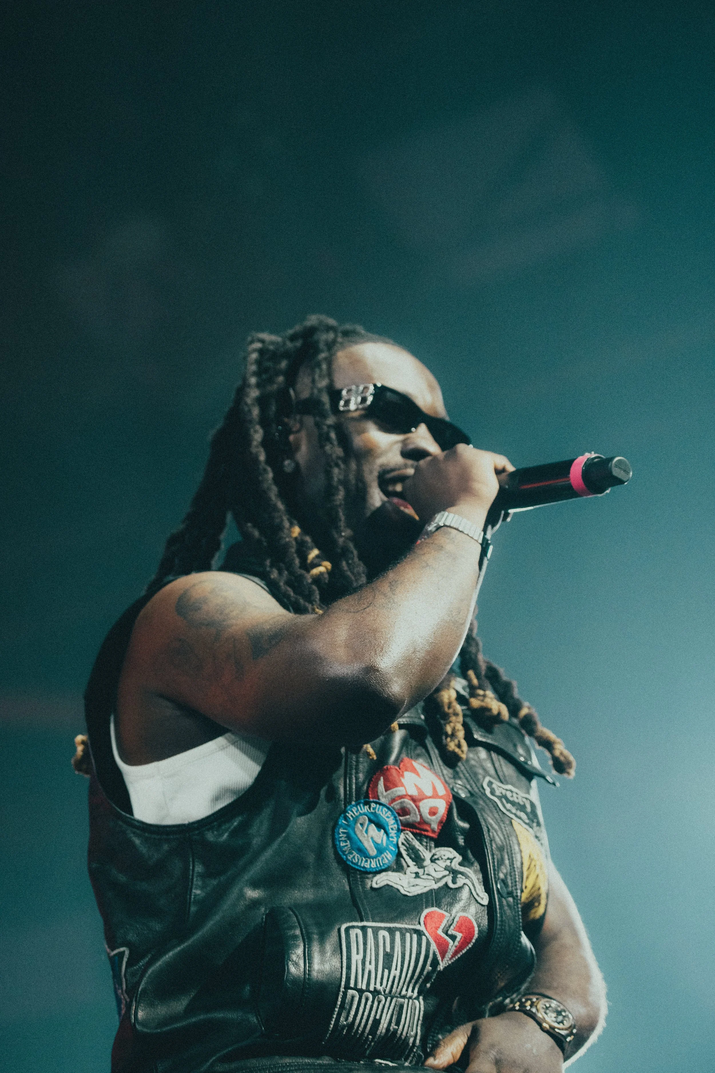 Un homme avec des dreadlocks, portant des lunettes de soleil, chantant dans un micro lors d'une performance sur scène.