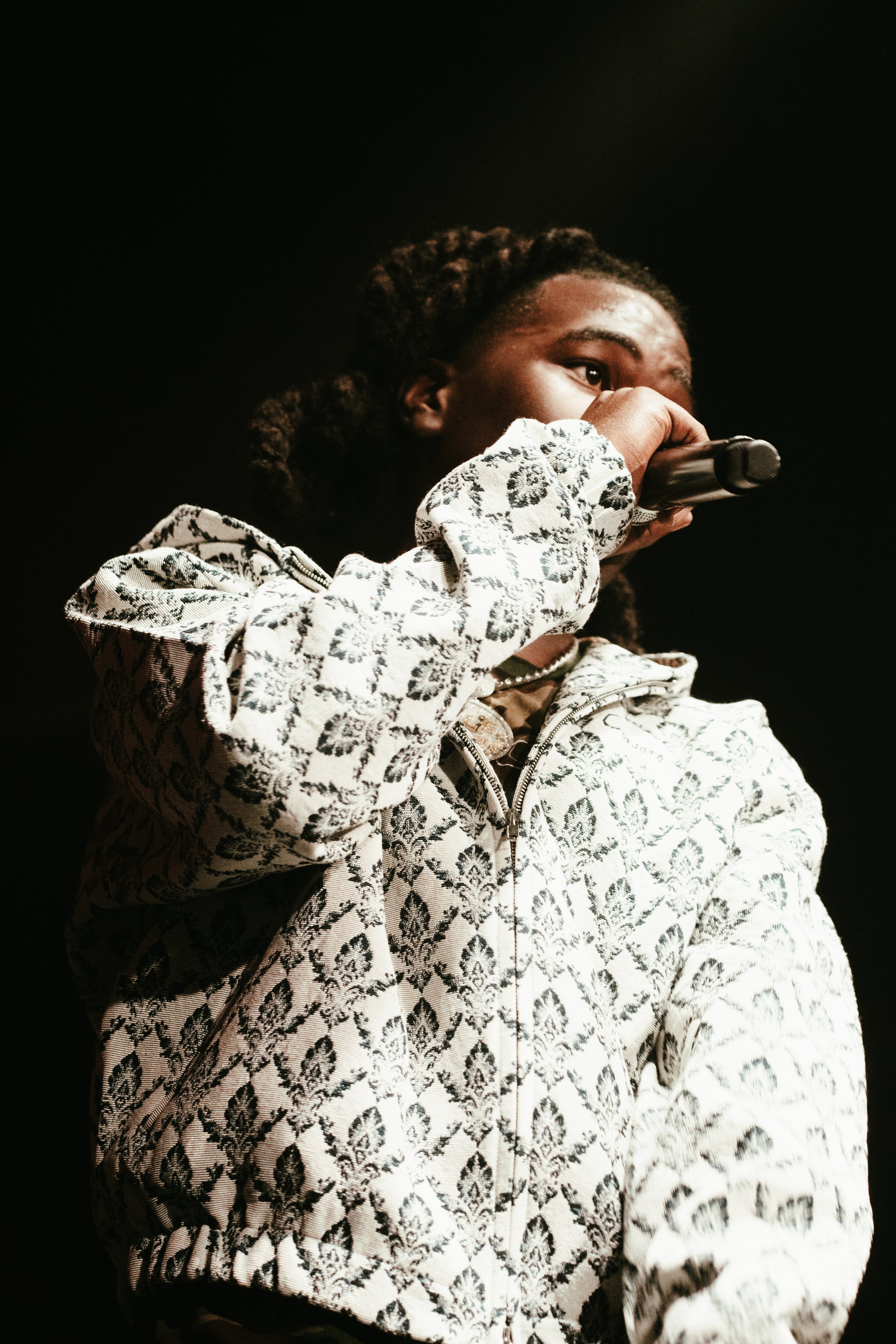 Une personne noire tenant un microphone et portant un sweat à motif noir et blanc.