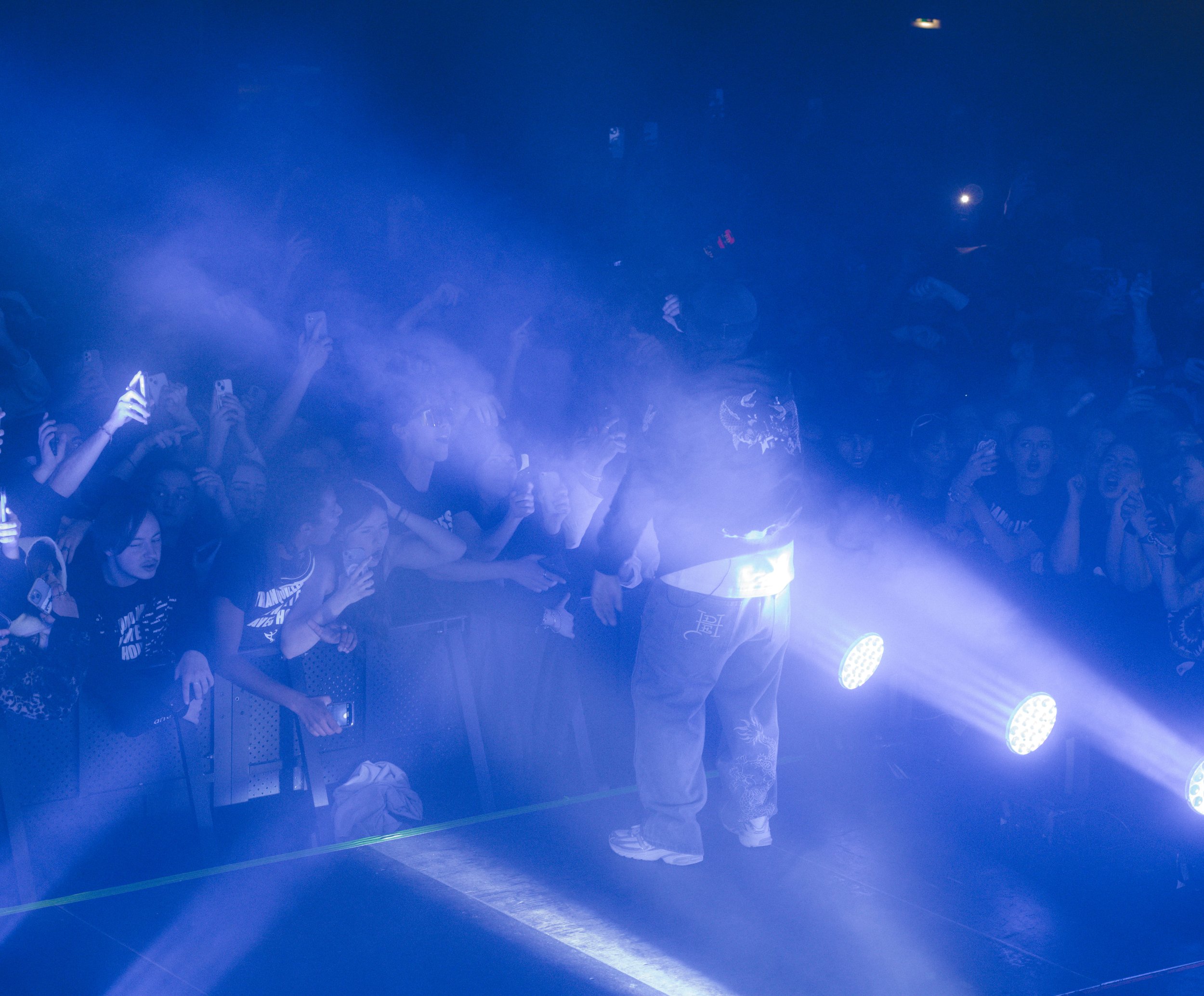 Foule de personnes dans un concert, illuminées par des projecteurs bleus, certaines prennent des photos ou filment avec leurs téléphones.