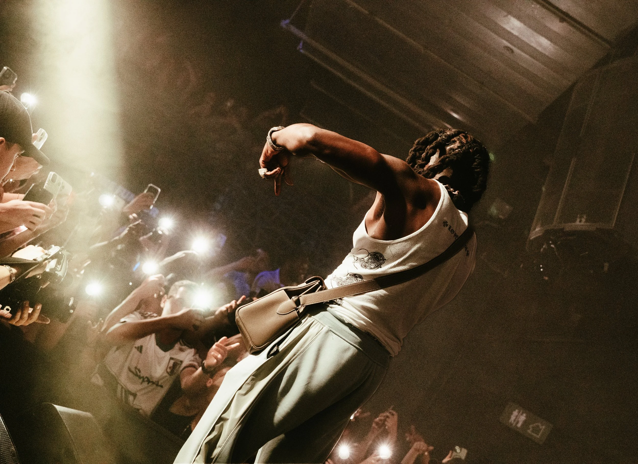 Une artiste sur scène lors d'un concert, entourée de nombreux spectateurs avec des téléphones allumés.