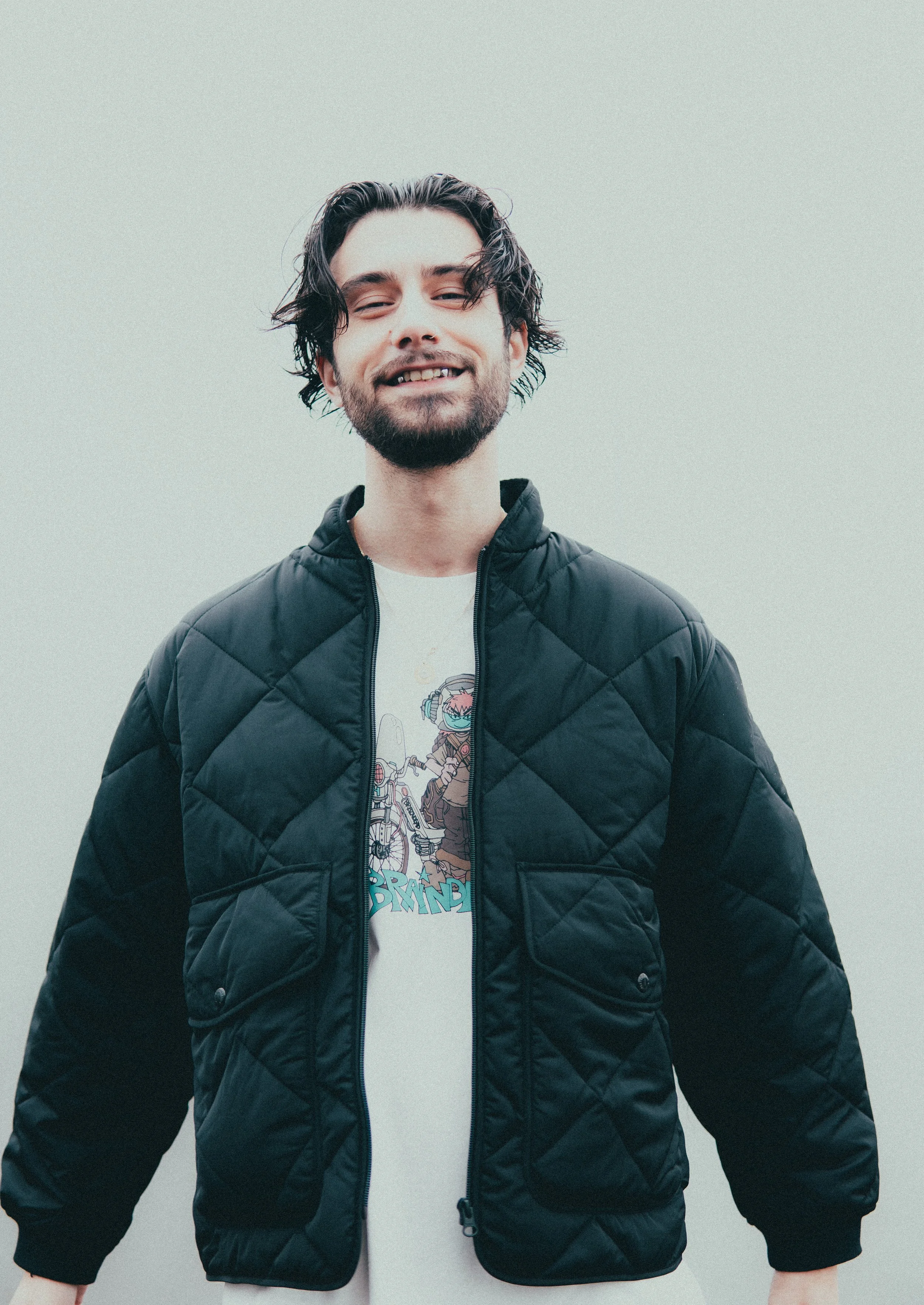 Jeune homme souriant portant une veste noire en quilting et un t-shirt avec un dessin de personnage en bike.