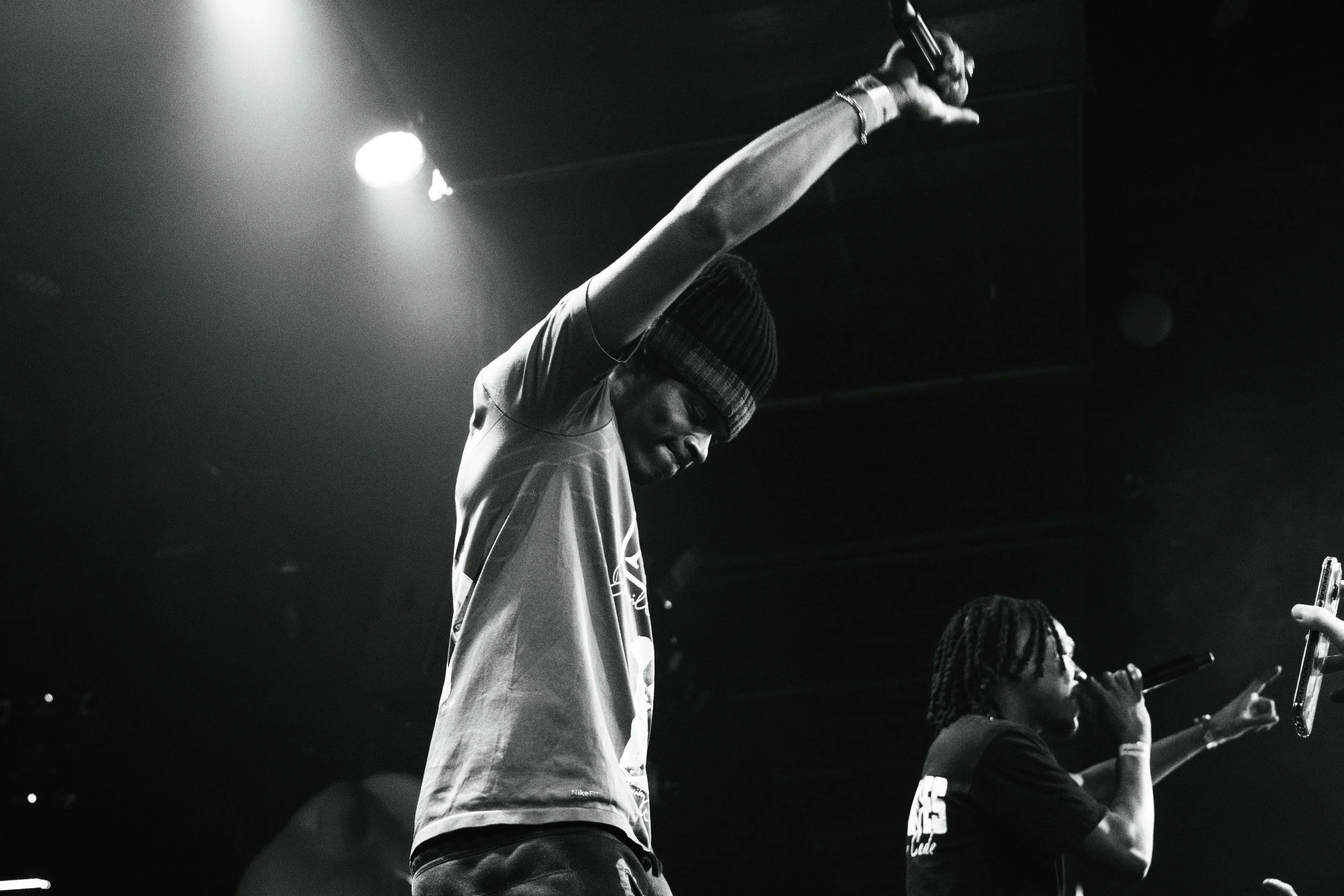 Deux artistes de rap sur scène, un homme en t-shirt et un bonnet, et une femme en t-shirt, tenant un microphone.