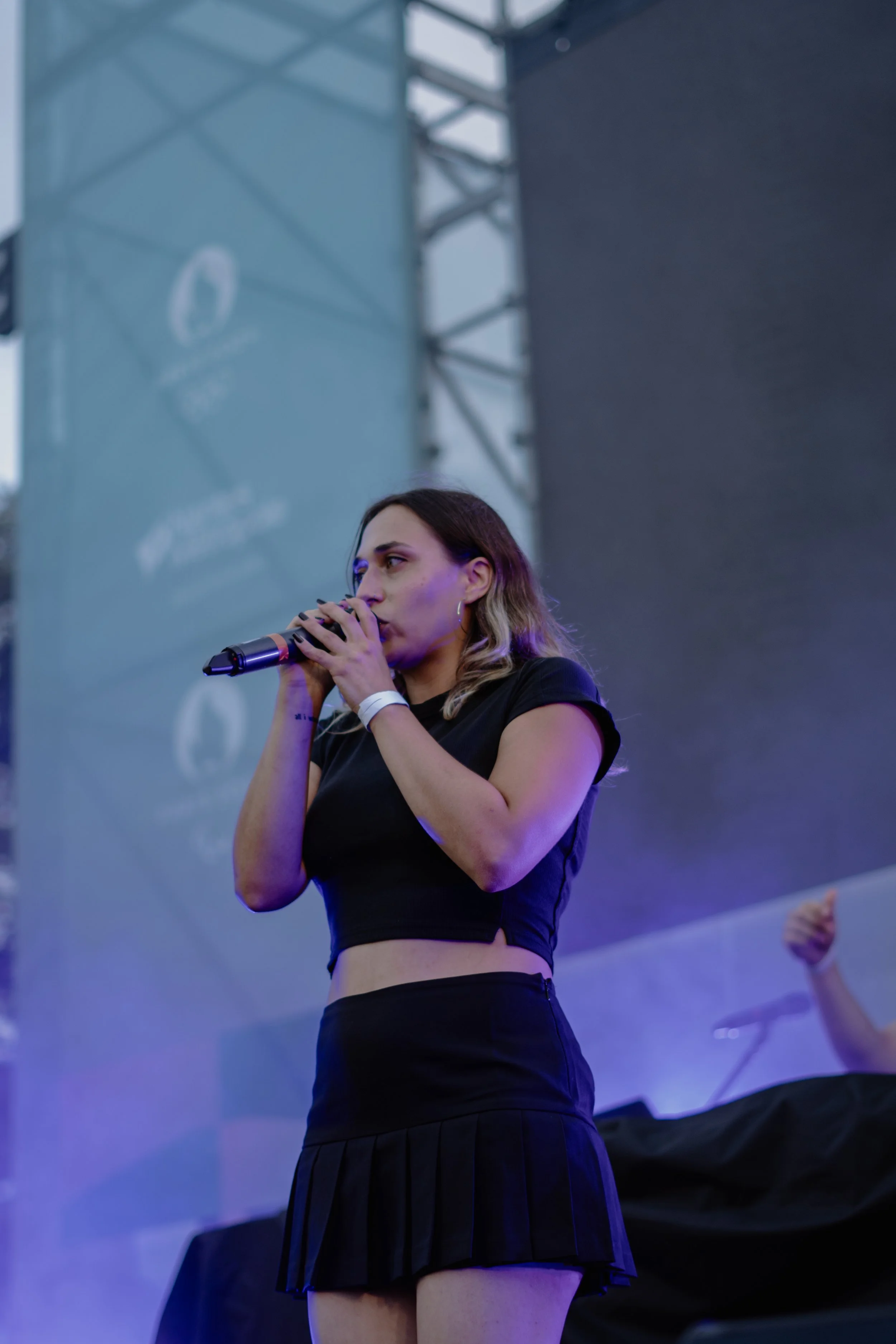 Jeune femme chantant dans un micro sur scène lors d'un événement en plein air, arrière-plan avec structures métalliques et écran