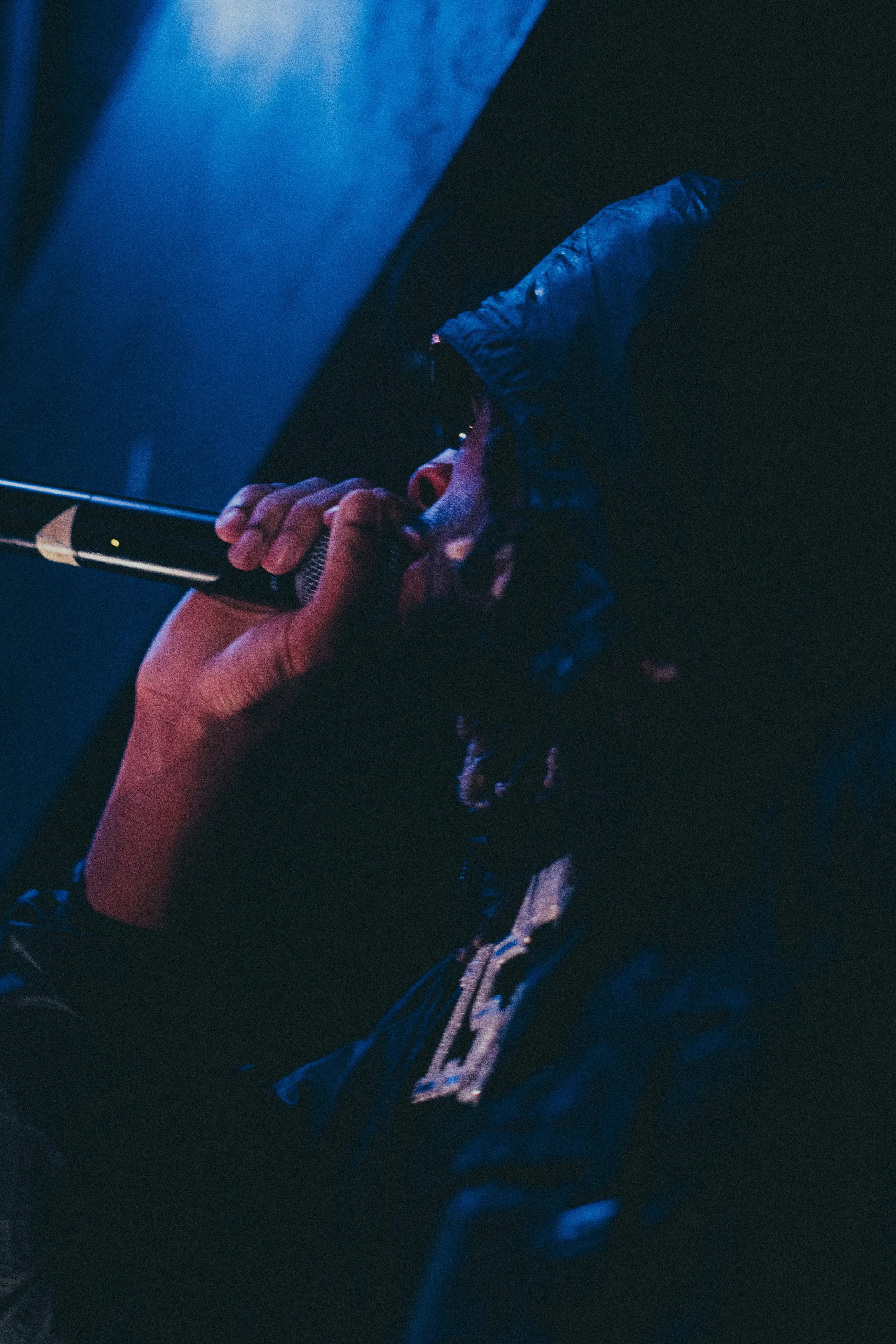 Une personne tient un microphone noir avec une main, dans un environnement sombre et éclairé par une lumière bleue.