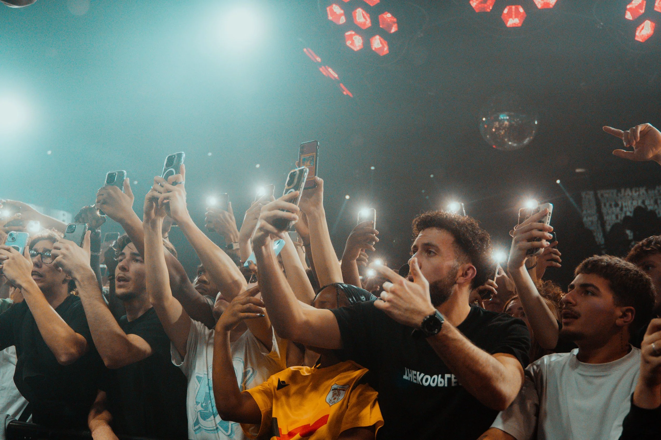 Une foule de spectateurs au concert, tous tenant des téléphones portables allumés, avec des lumières brillantes et un plafond décoré de néons rouges, enregistrement un événement en direct.