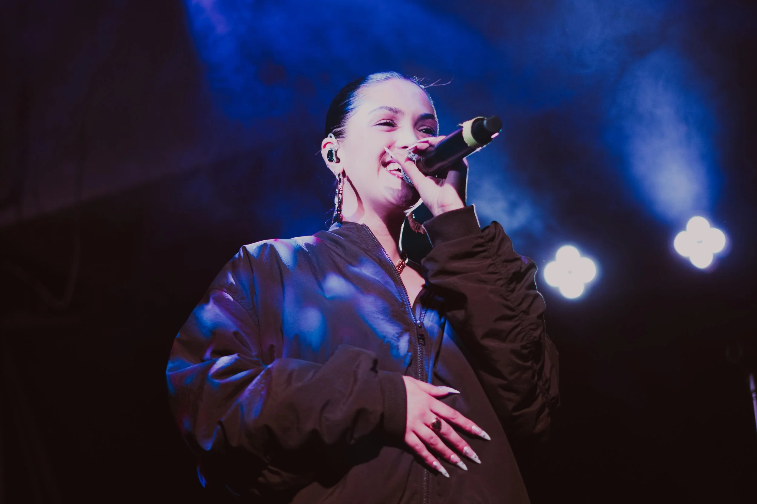 Une femme chante lors d'un concert, tenant un micro avec un éclairage coloré en arrière-plan.