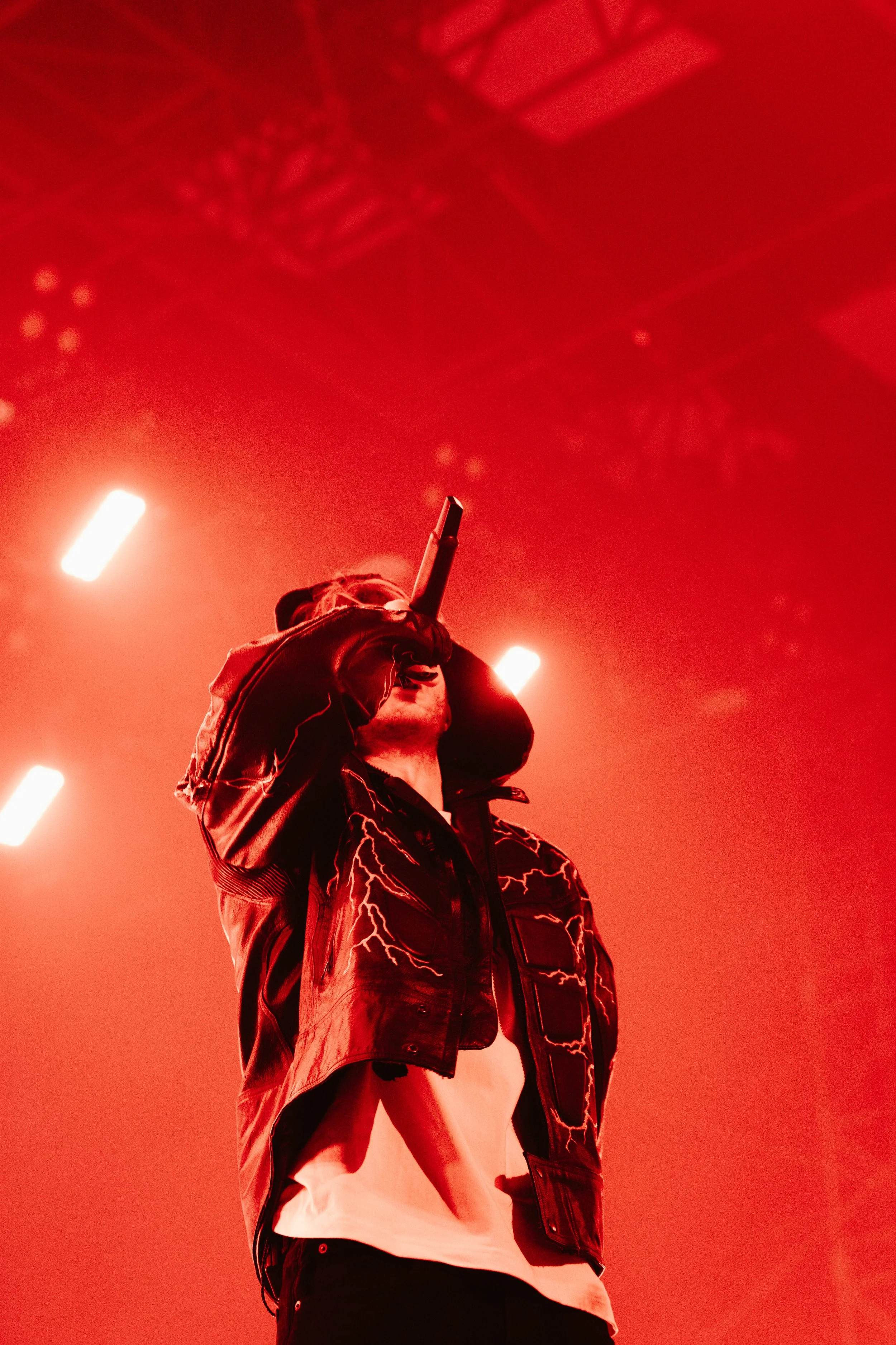 Un chanteur en costume noir avec des éclairs lumineux rouges en arrière-plan, lors d'une performance scénique.