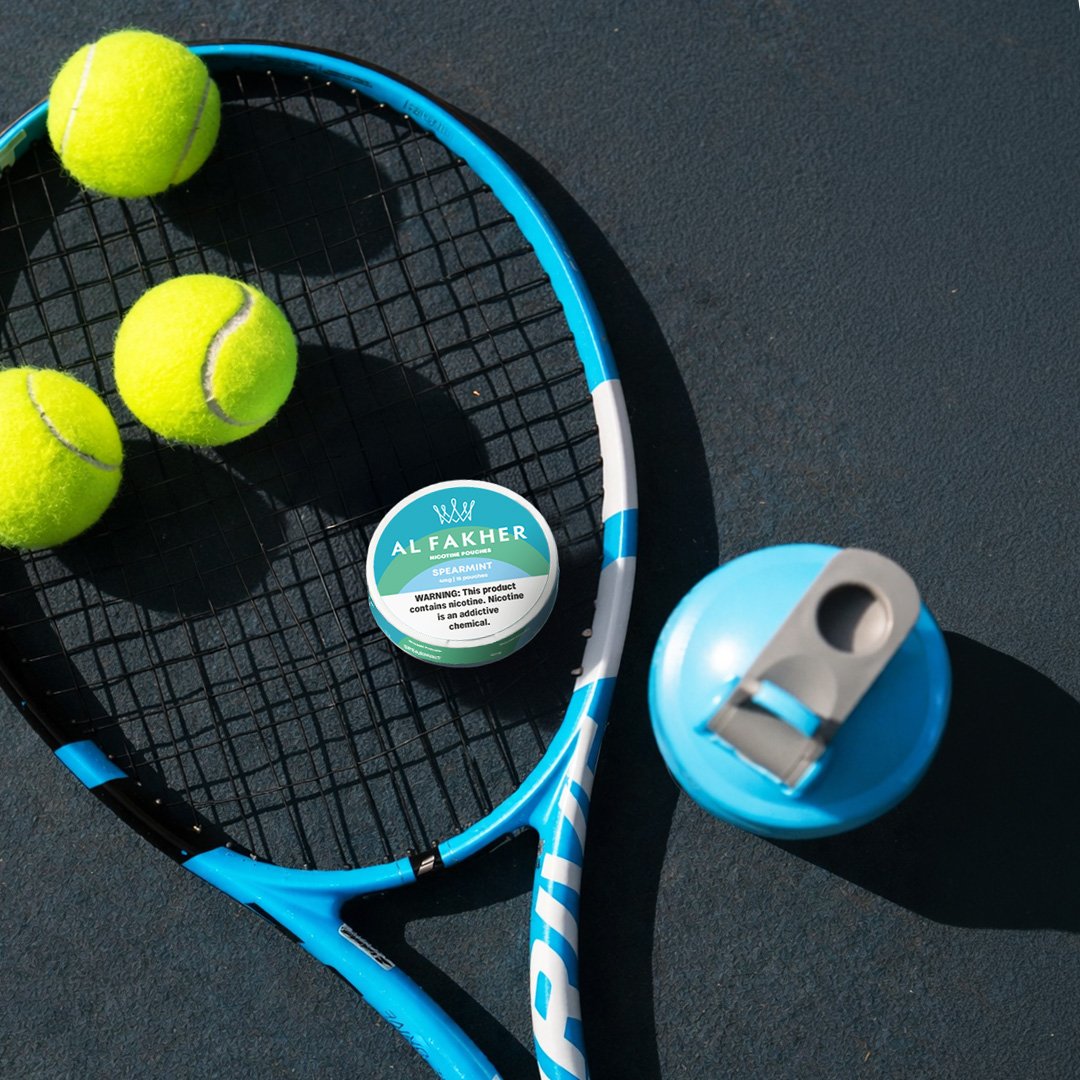 Al Fakher Spearmint Nicotine Pouches can placed on a tennis racket beside tennis balls.