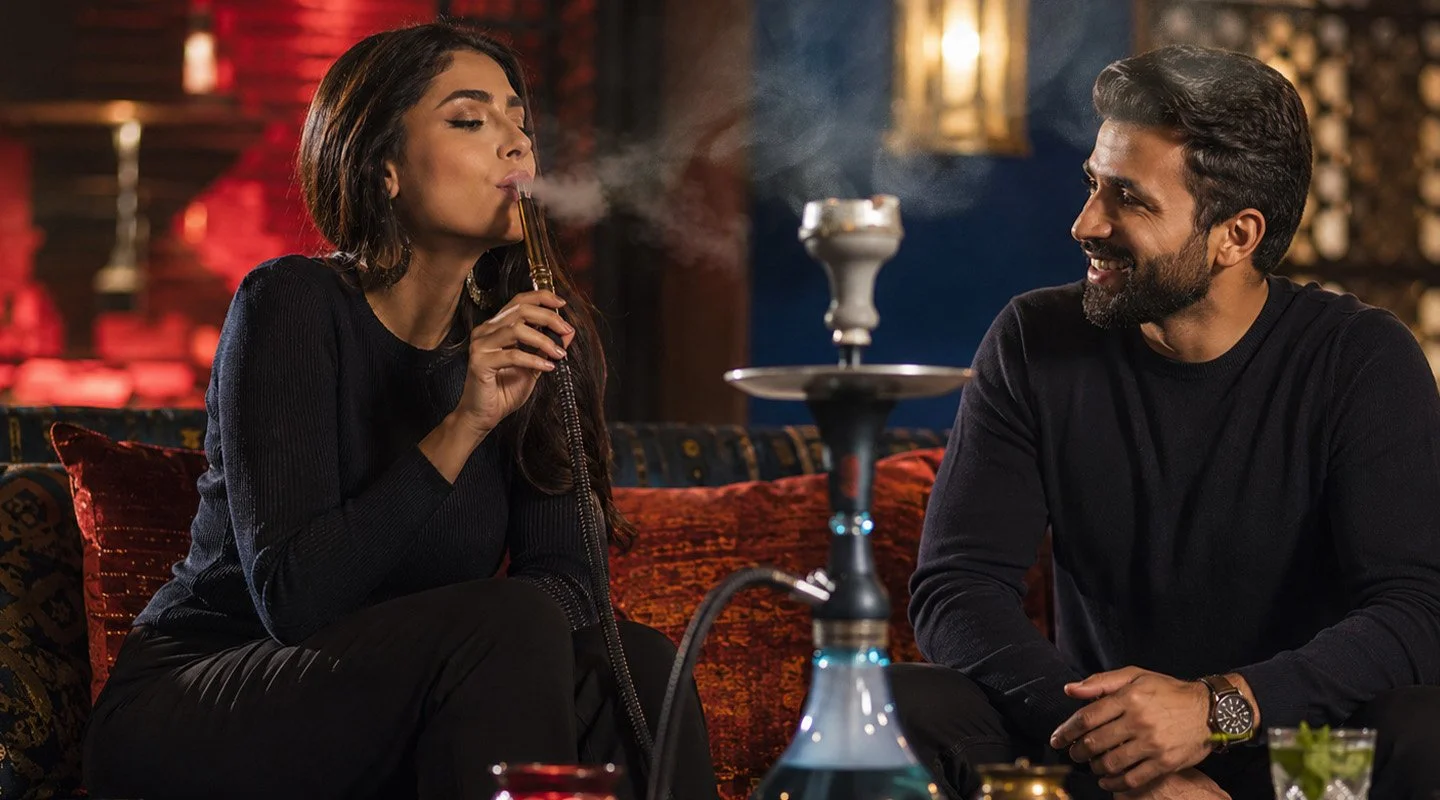A female smoking hookah while a male is seated beside her in a lounge
