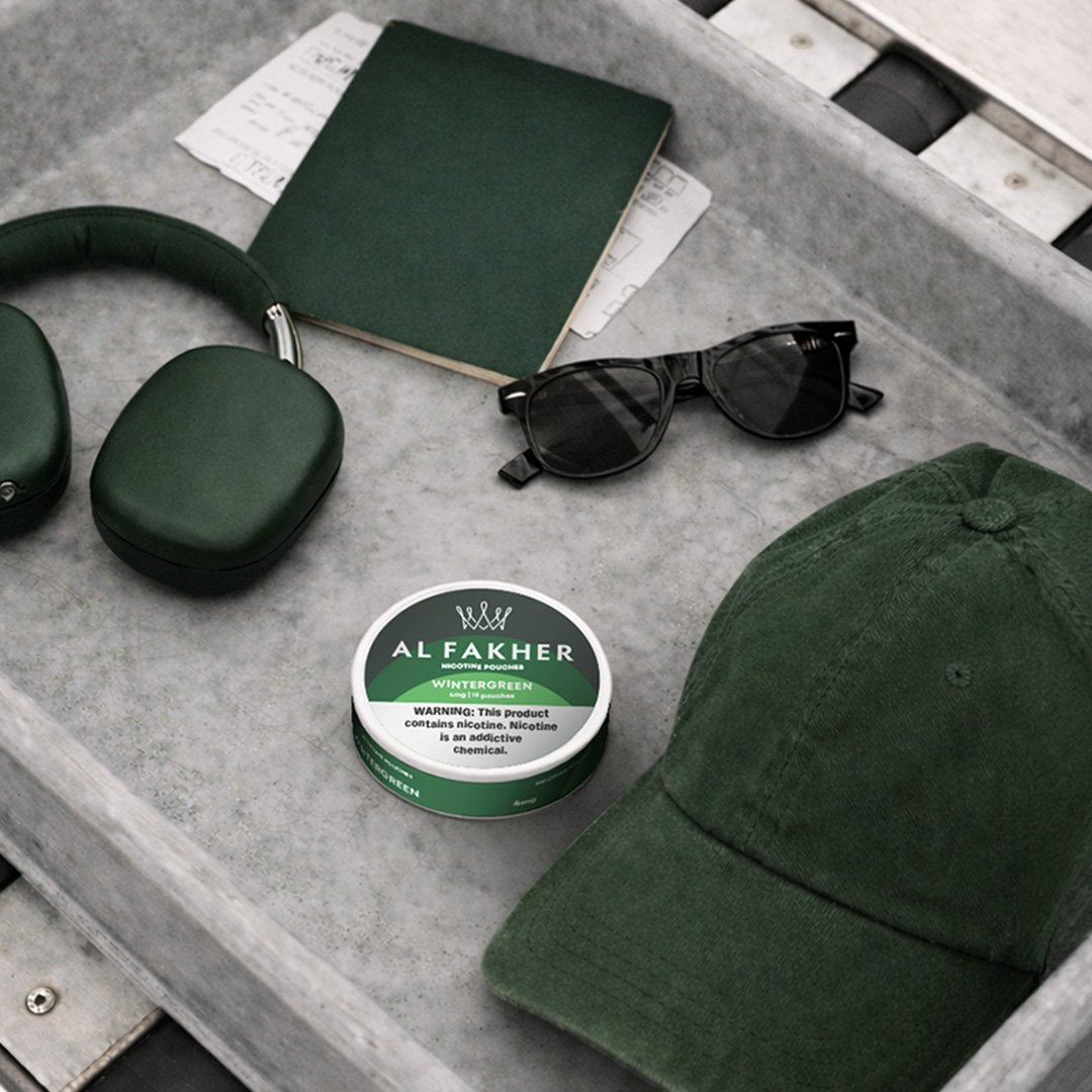 Al Fakher Wintergreen Nicotine Pouches can displayed with sunglasses, headphones, and a green cap.