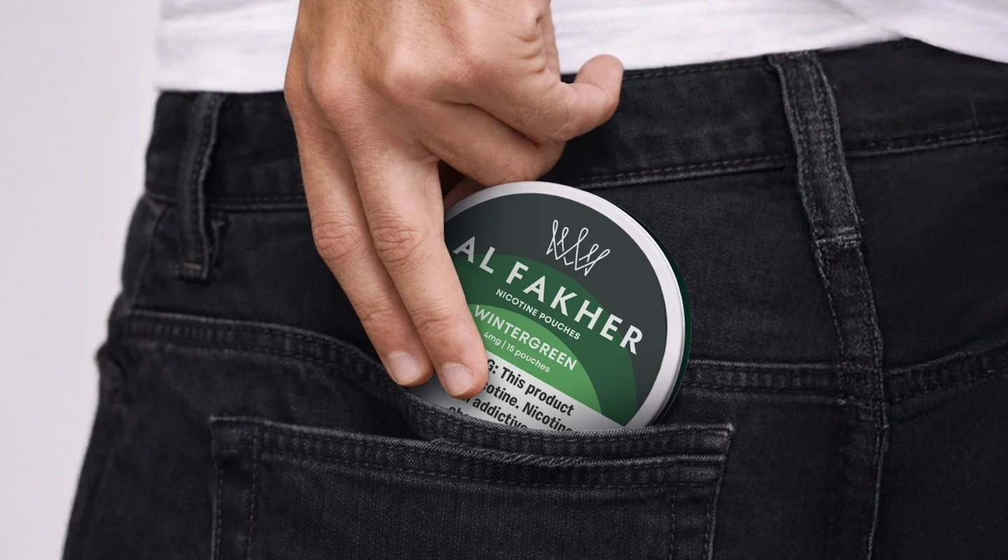 Hand placing an Al Fakher Wintergreen Nicotine Pouches can into a jeans pocket.