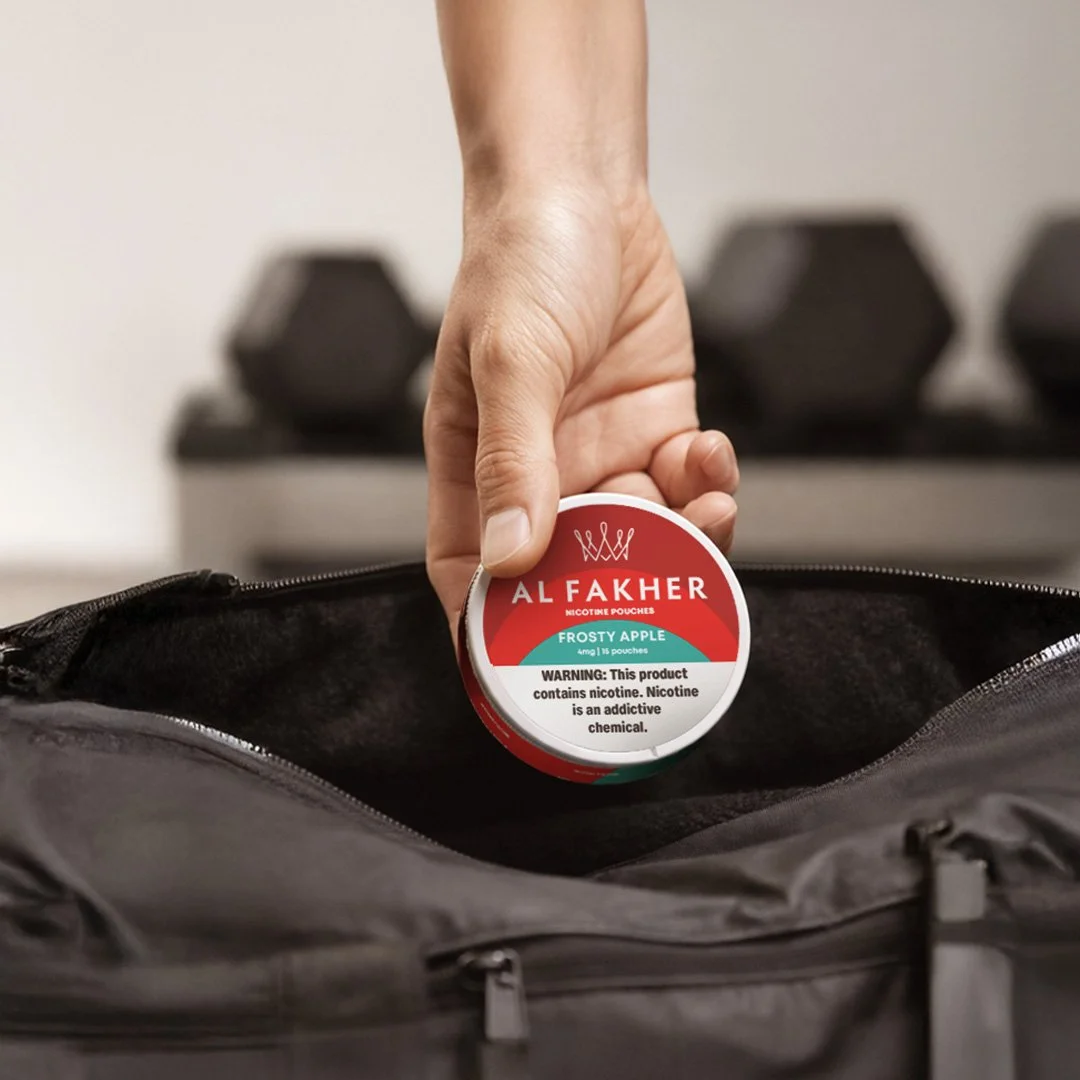 Hand placing an Al Fakher Frosty Apple Nicotine Pouches can into a black bag.