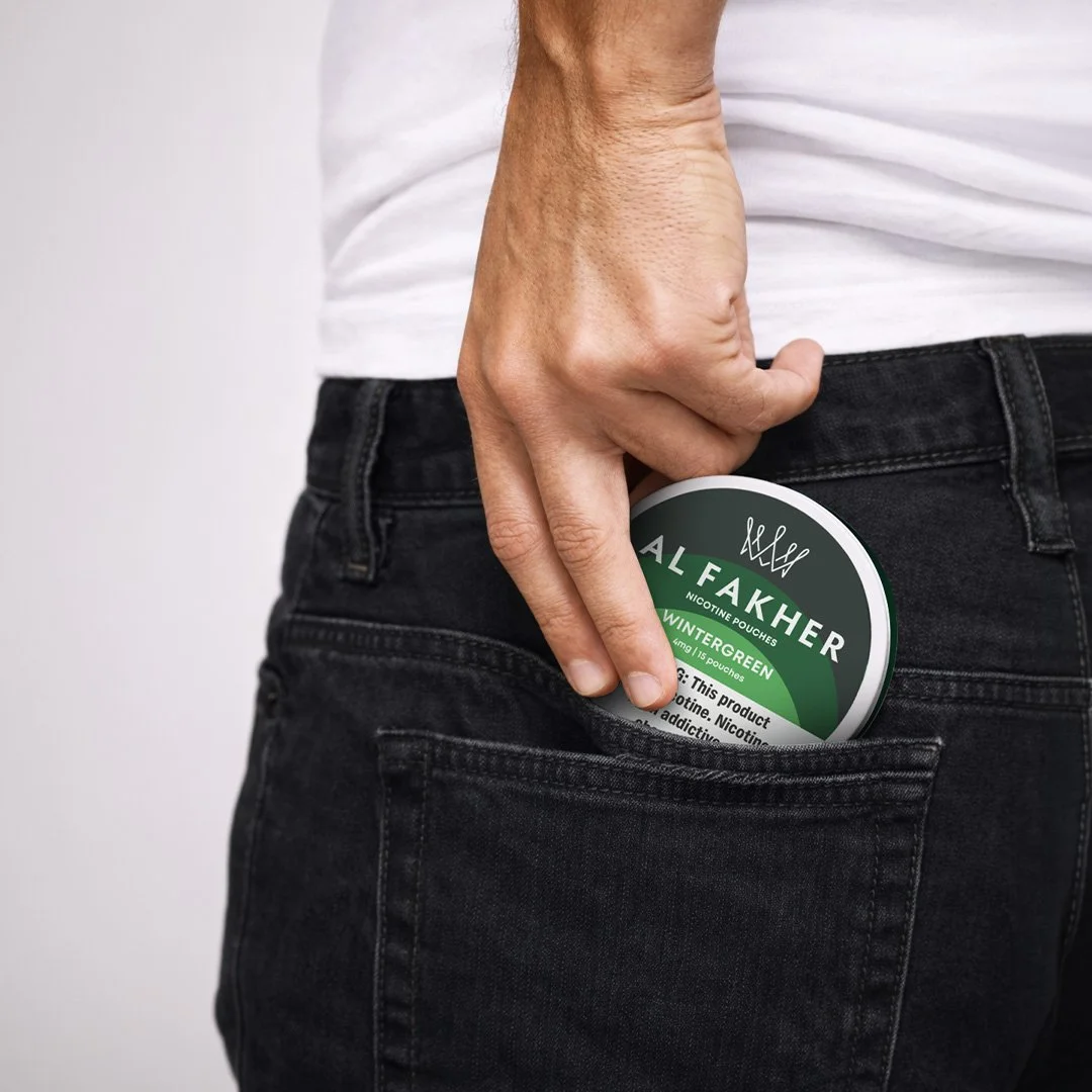 Hand placing an Al Fakher Wintergreen Nicotine Pouches can into a back pocket.