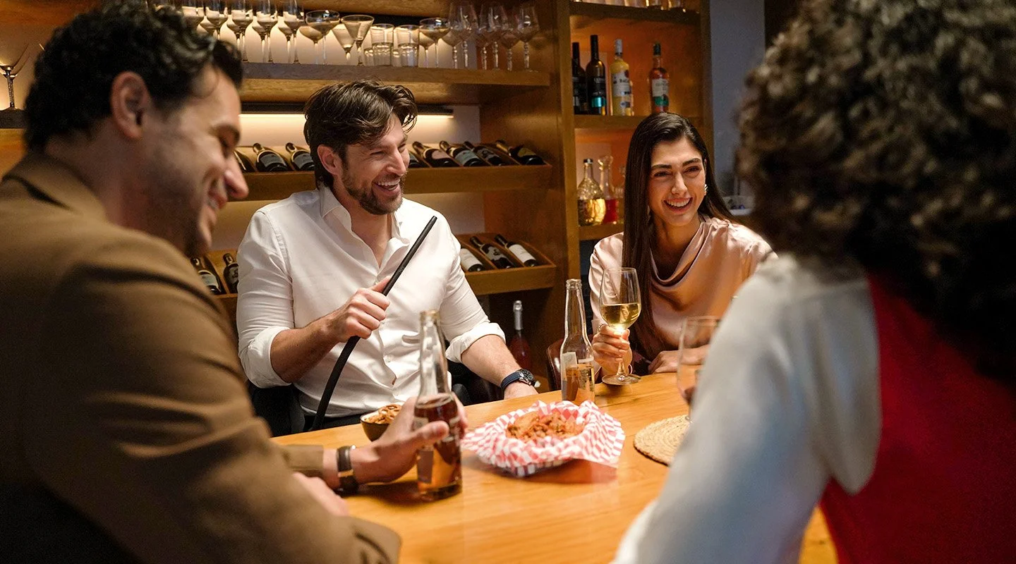 Friends sharing a relaxed evening in a lounge, enjoying drinks, food, and conversation around a table with a shisha pipe.
