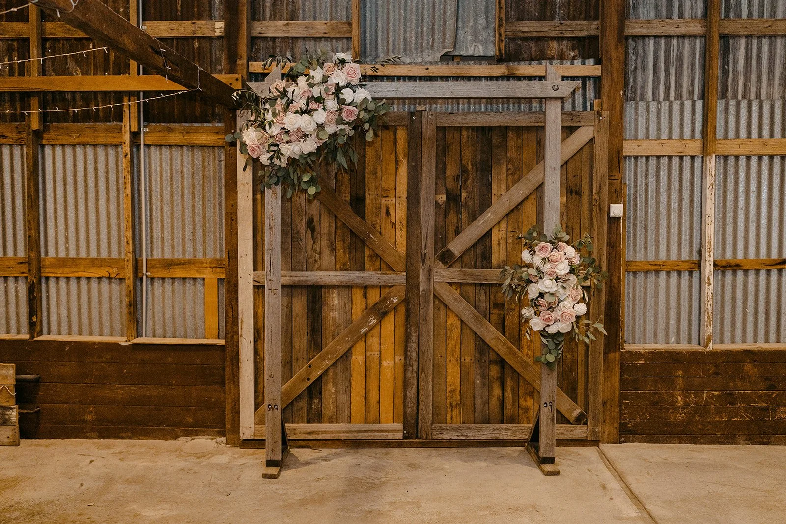 Wood barn door decorated with pink and white roses and greenery in an indoor rustic setting.