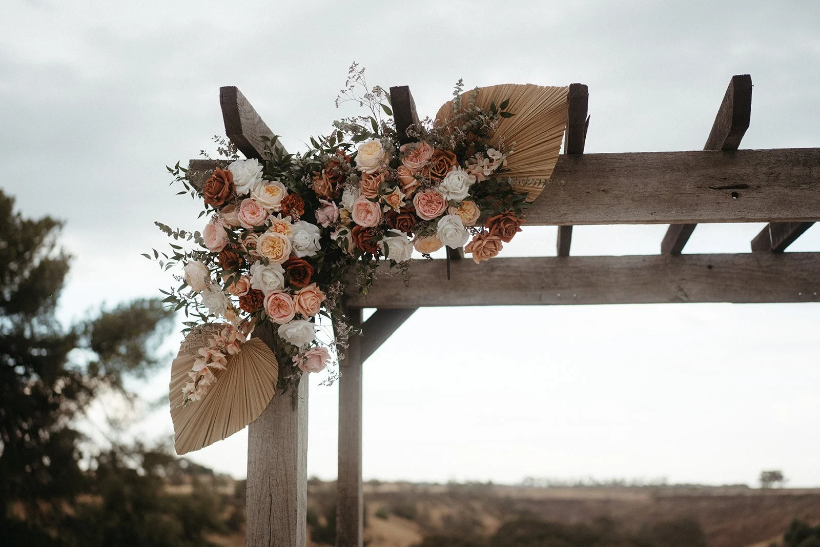 A floral arrangement on a wooden outdoor structure with a cloudy sky background.
