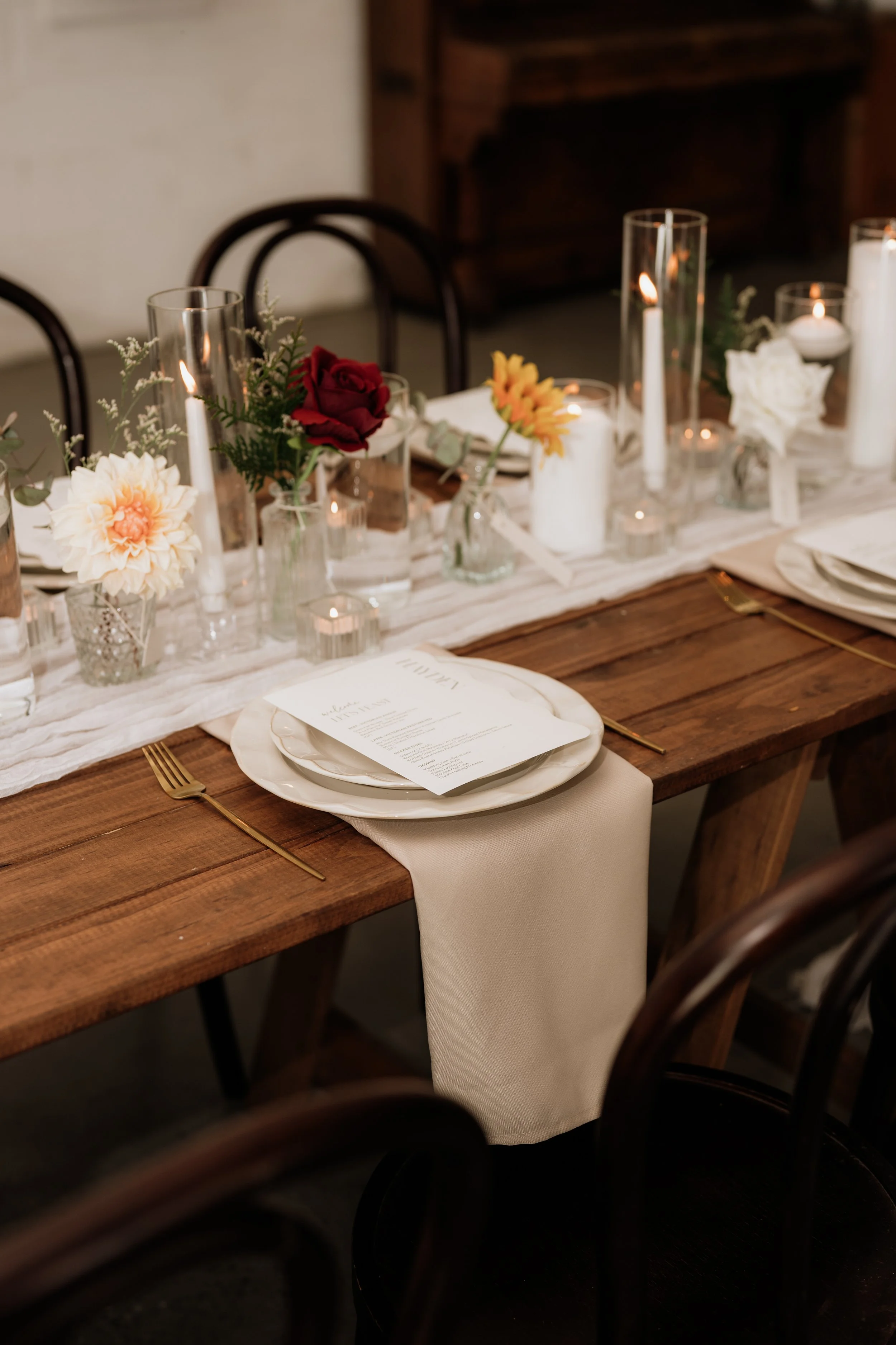 Elegant wooden dining table decorated with candles, flowers, and tableware for a formal event.