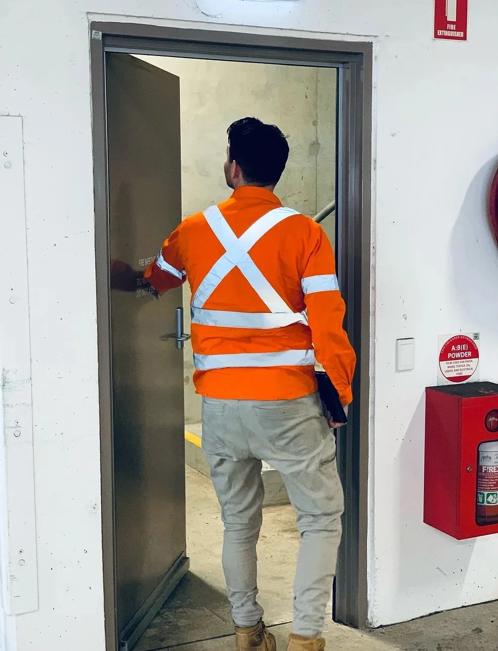Person in orange safety vest entering a stairwell door in a building