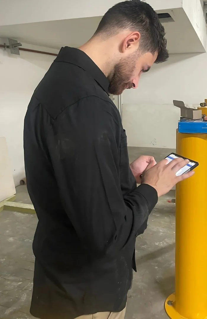 Person wearing a black shirt looking at a smartphone in a workshop setting with industrial equipment around.