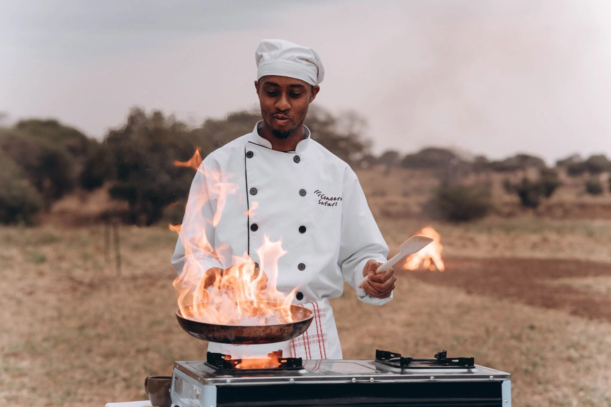 Luxury safari bush breakfast setup under a tree in the African savannah with 4x4 vehicle and scenic wilderness views.