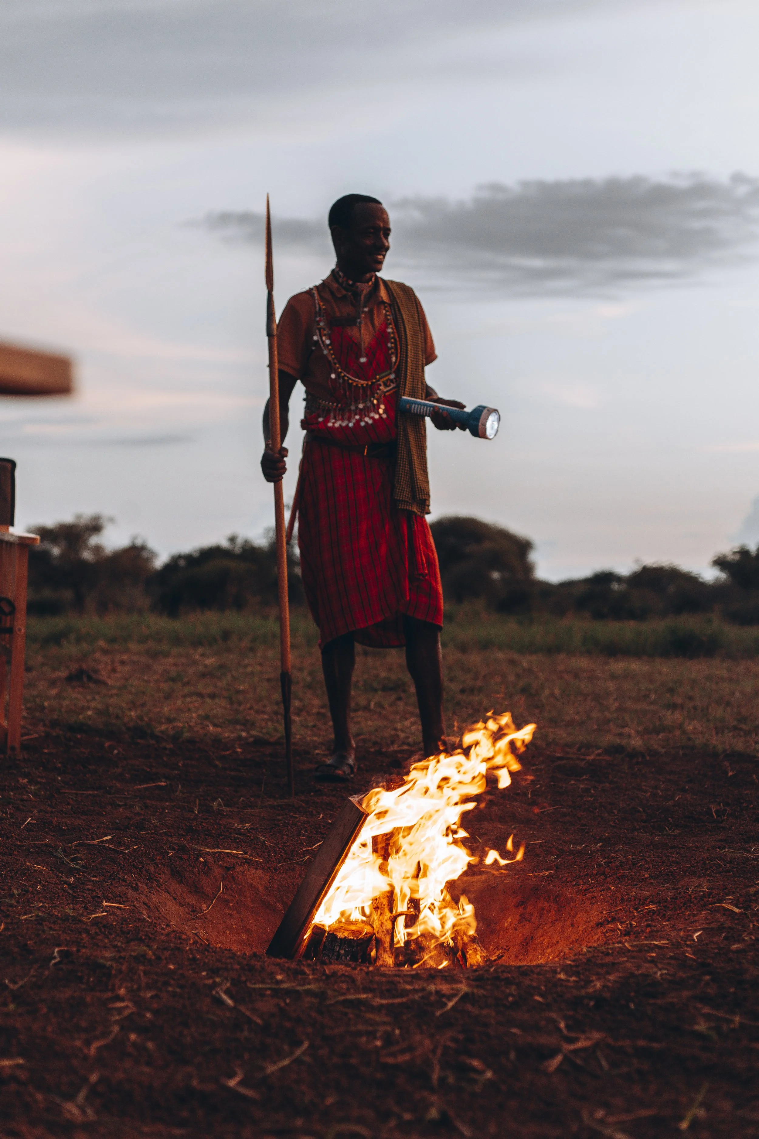 Safari camp bonfire surrounded by chairs at sunset in the African bush, offering guests a luxury wilderness experience.