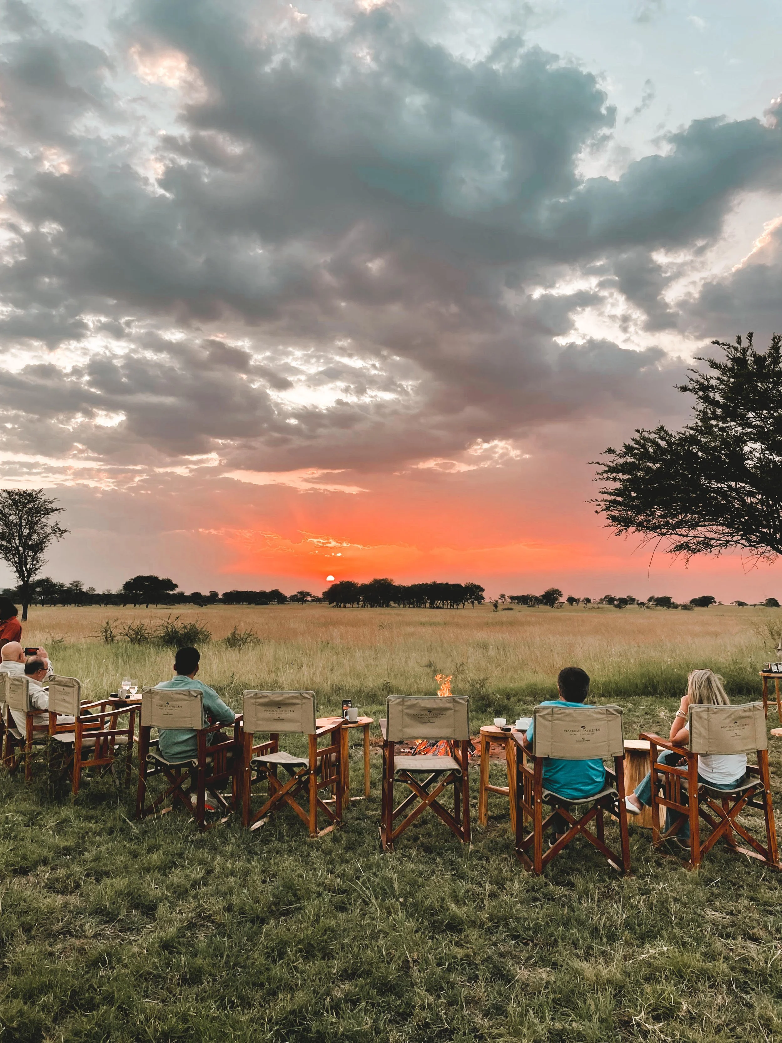 Safari camp bonfire surrounded by chairs at sunset in the African bush, offering guests a luxury wilderness experience.