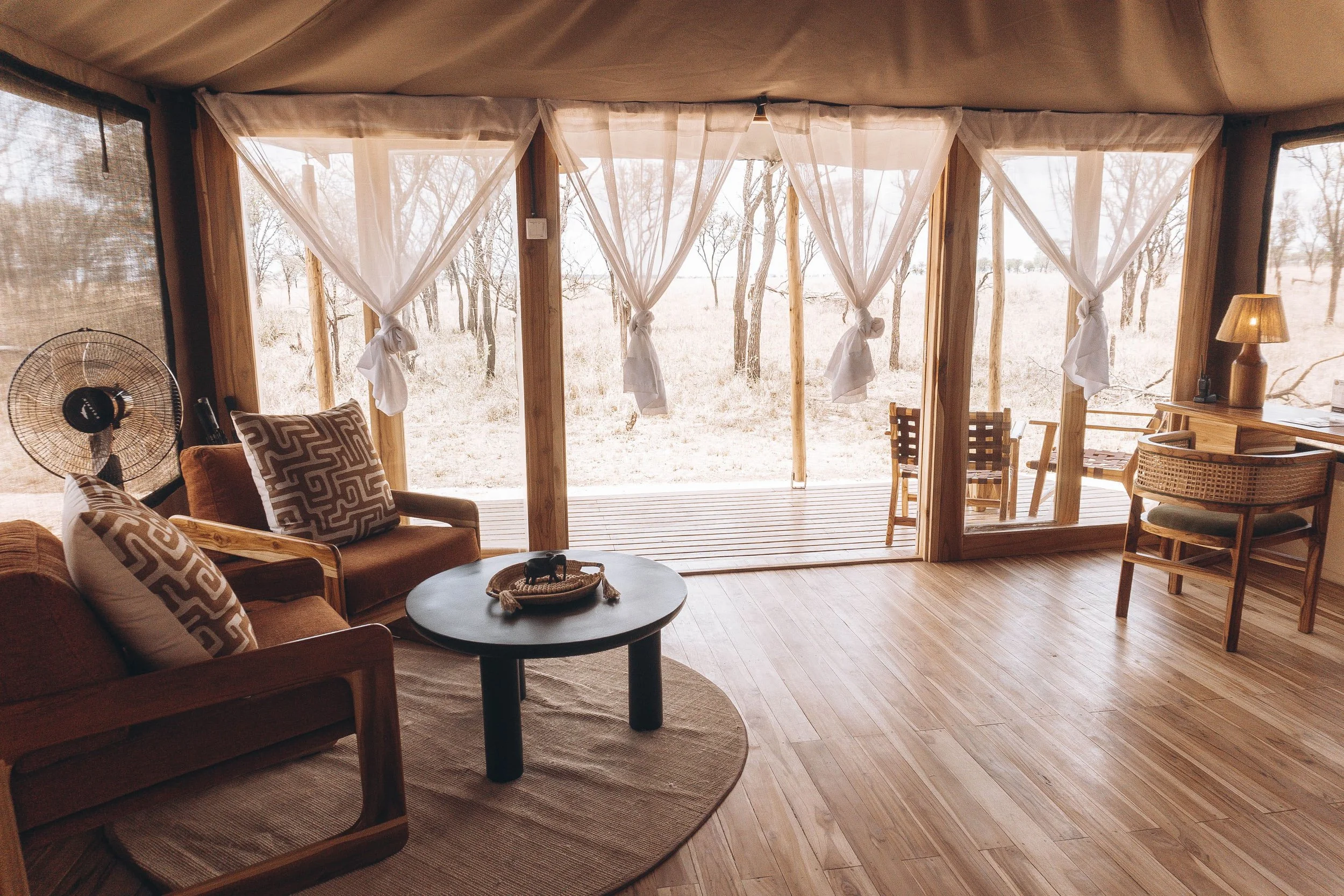 Luxury safari tent bedroom with natural wood furniture, African-inspired decor, and cozy bedding for an elegant wilderness stay.