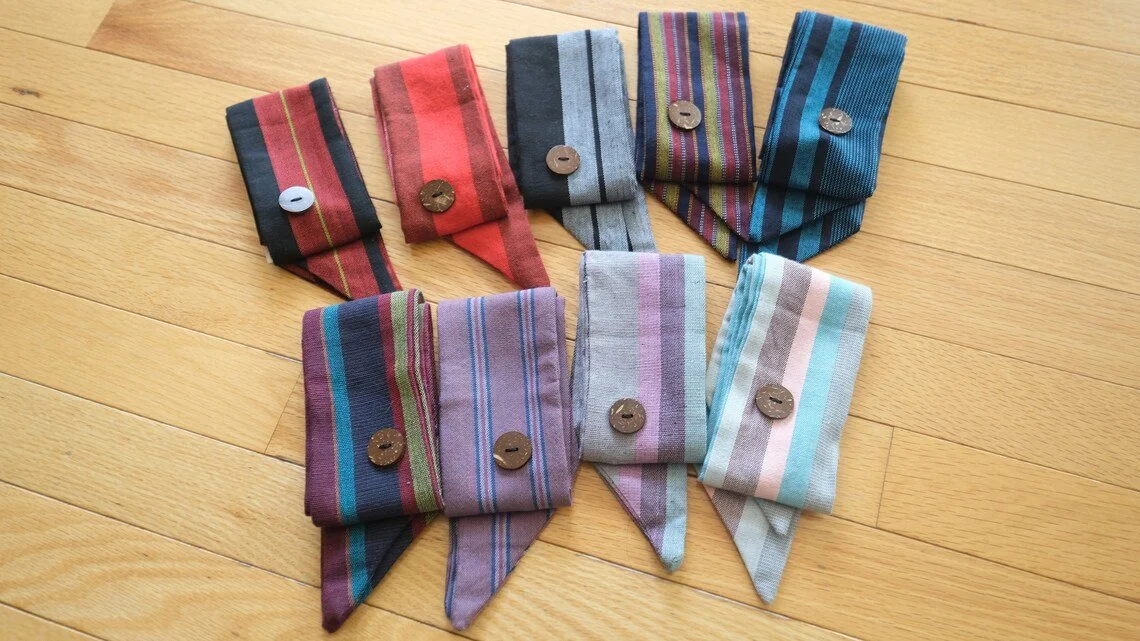A collection of nine colorful striped sock cuffs with buttons on a wooden floor.