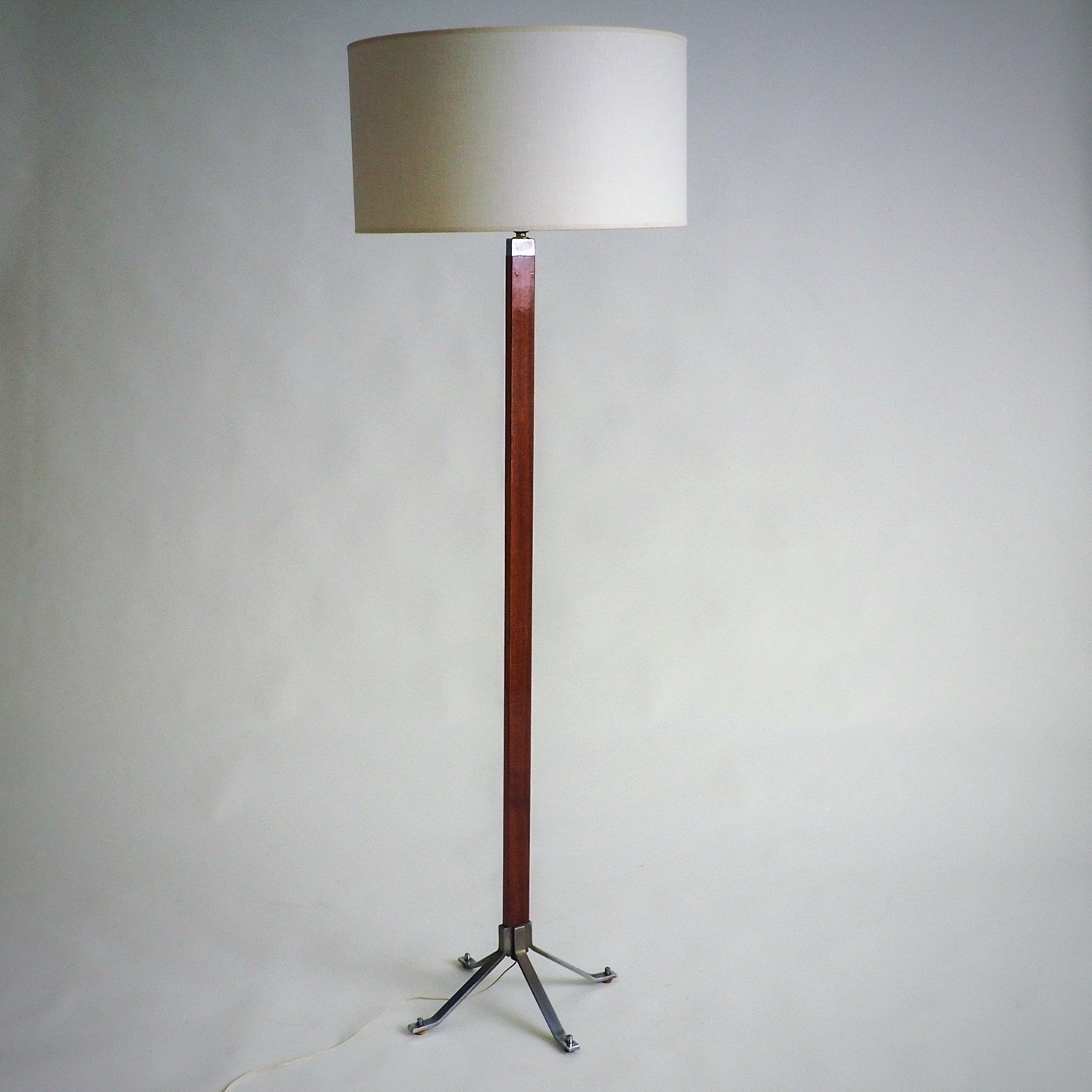 (SOLD)

This elegant vintage floor lamp embodies a timeless mid-century aesthetic. 

The tall, slender stand, crafted from a warm-toned polished wood, is mounted on a striking cruciform base of brushed metal. The lamp is crowned with a classic, cylin