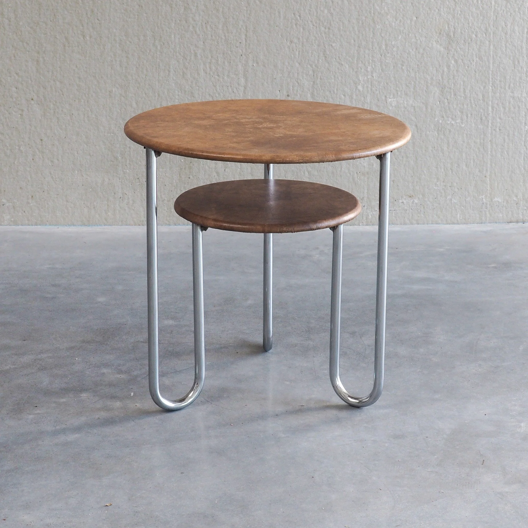Bauhaus Two-Tier Side Table with Leather Top

A crisp, functional Bauhaus-style side table featuring two circular tiers framed by continuous U-shaped tubular nickel legs. The minimalist geometric metal structure creates an airy, sculptural footprint.
